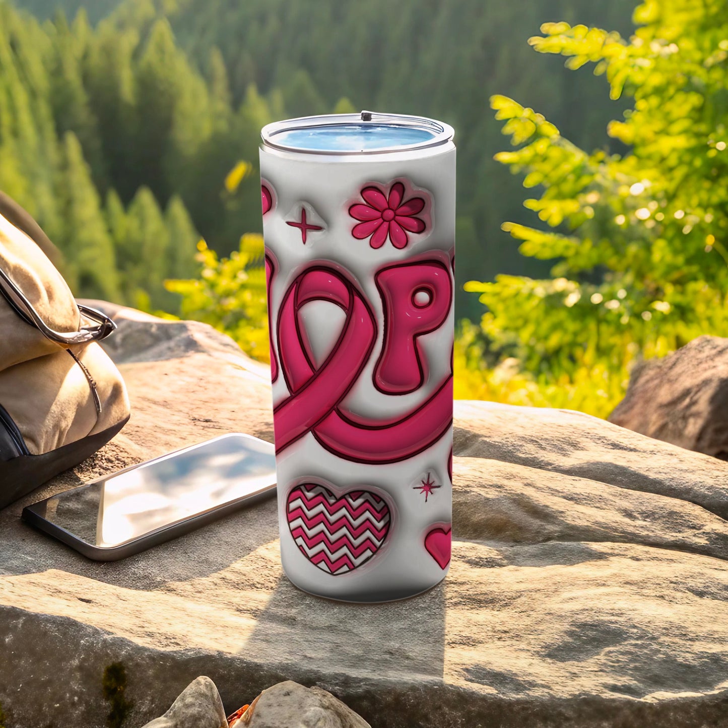 White tumbler with pink ribbon and heart designs rests on rocks.