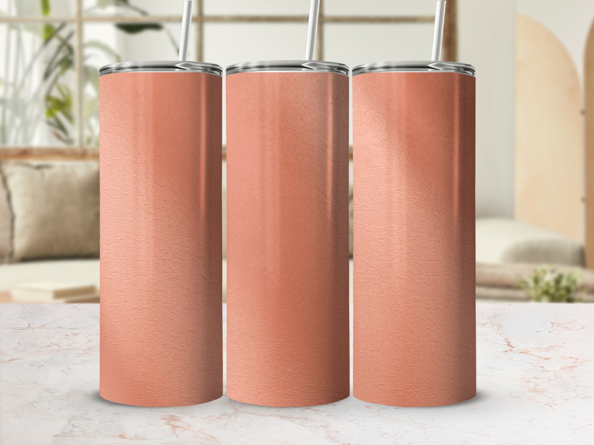 Three rose gold tumblers with silver lids and straws displayed on a marble surface.