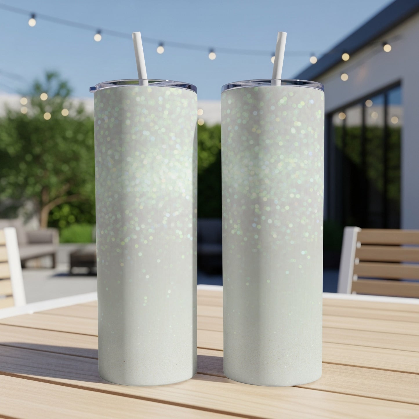 Two white glitter tumblers with straws on a wooden table outdoors.