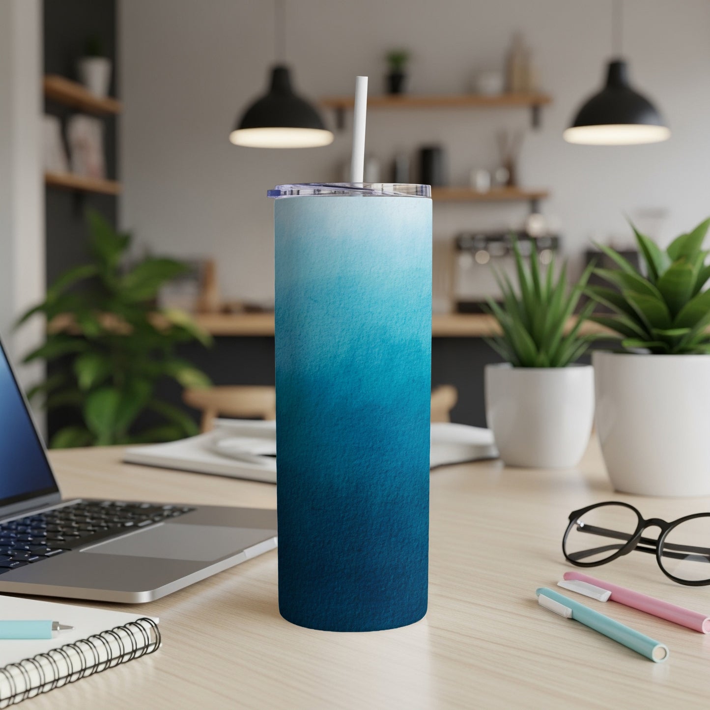 Blue ombre tumbler with straw on a wooden desk next to a laptop.