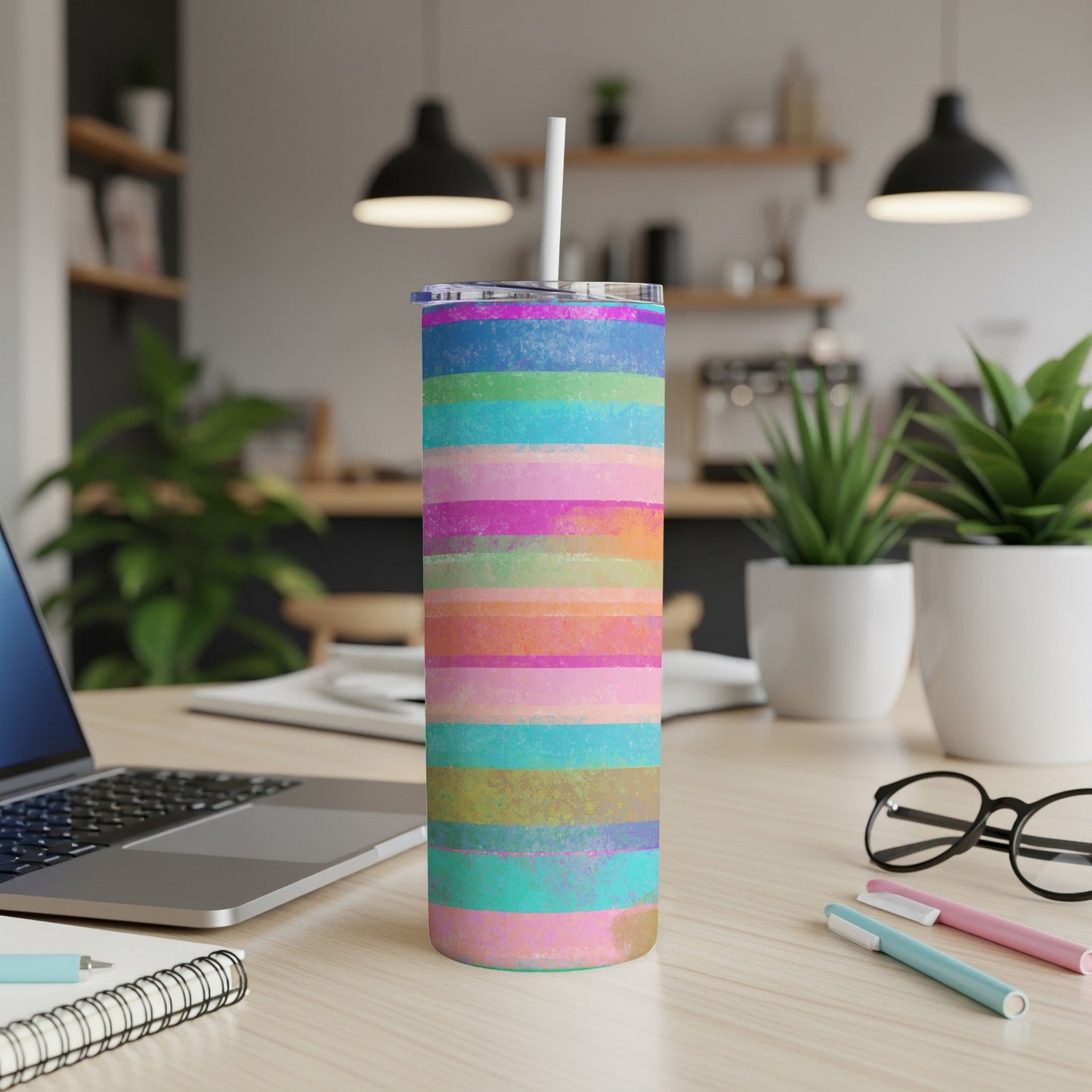 Tall tumbler with colorful horizontal stripes and a white straw on a desk.