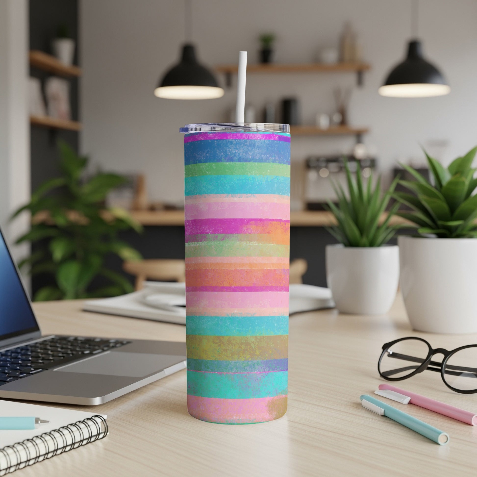 Tall tumbler with colorful horizontal stripes and a white straw on a desk.