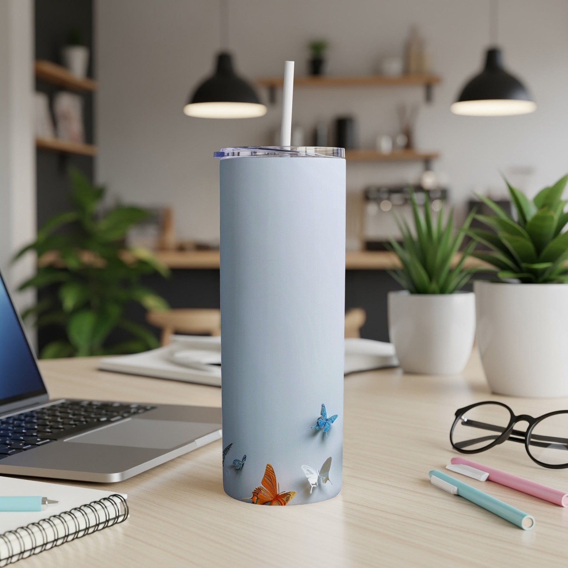 Light blue tumbler with butterflies on a desk with a laptop and pens.