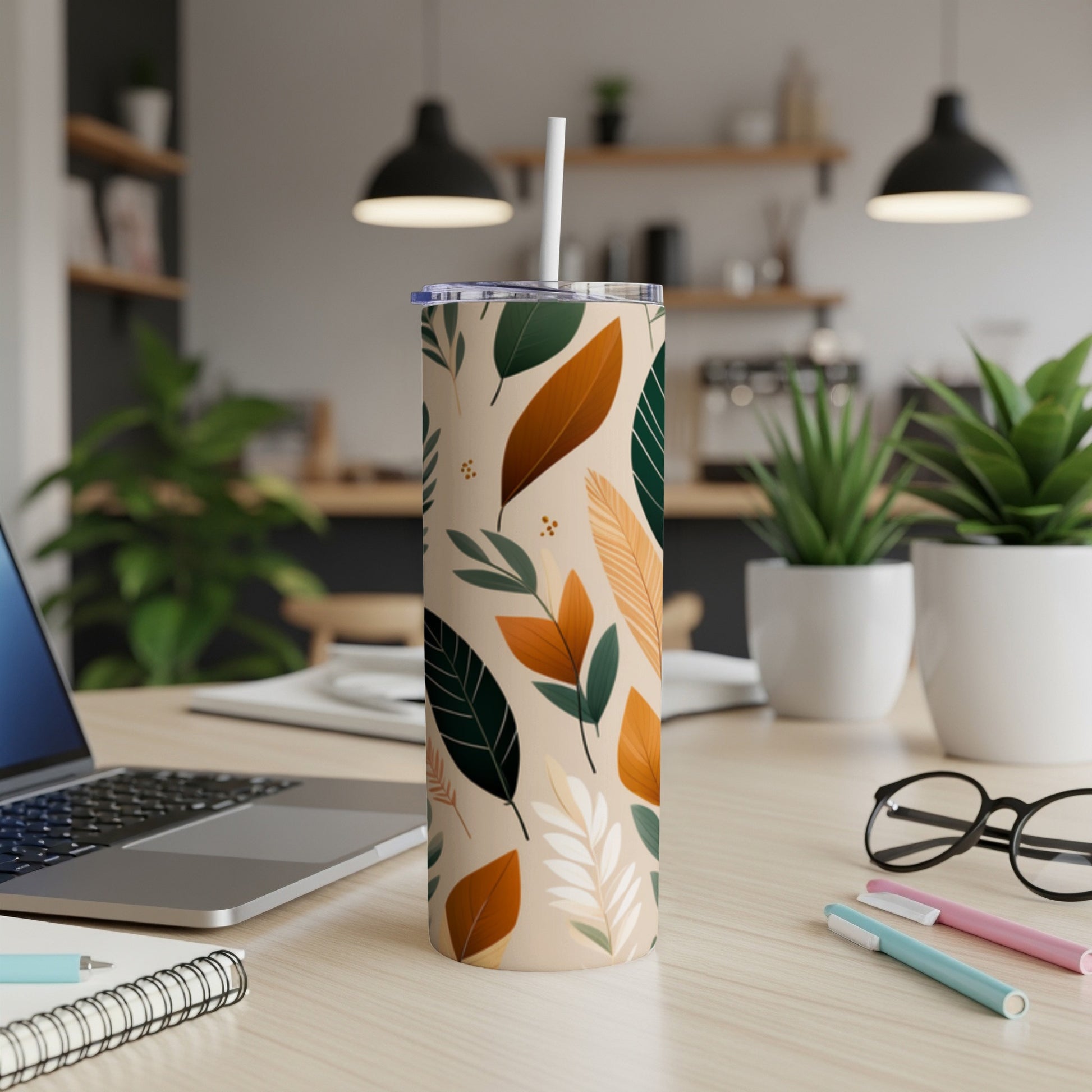 Tall tumbler with abstract leaf pattern, white straw, on a desk.
