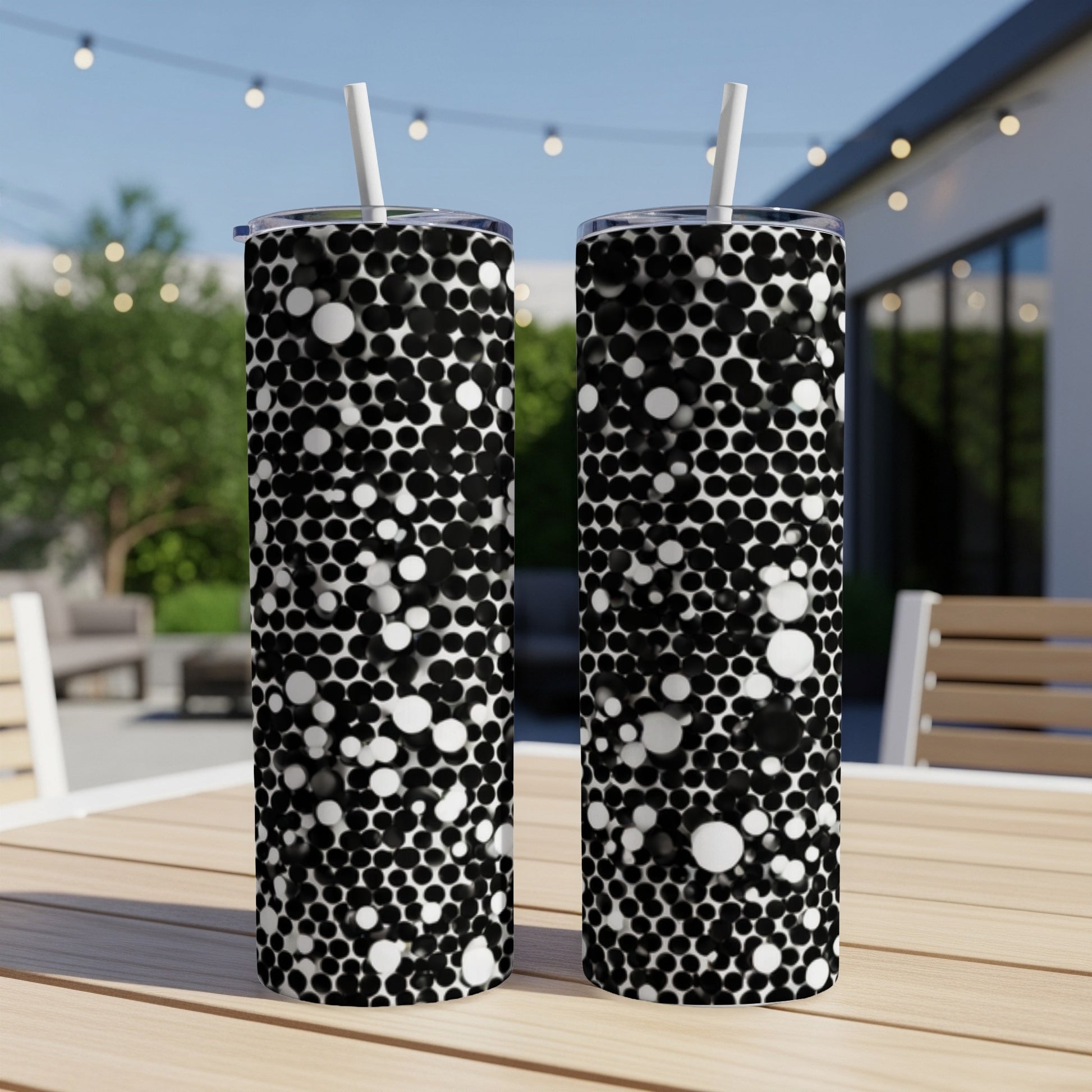 Two black and white speckled tumblers with straws on a table.