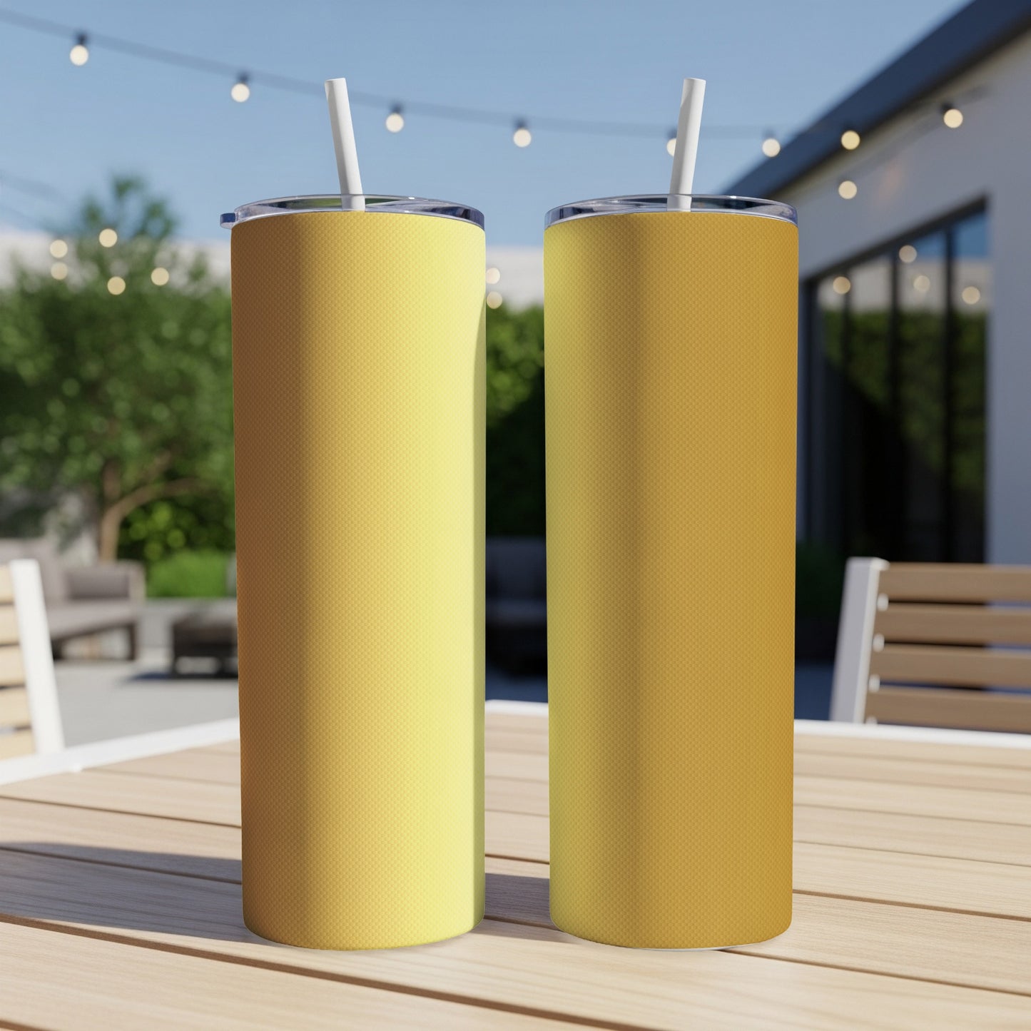 Two gold patterned tumblers with straws sit on a wooden table outdoors.