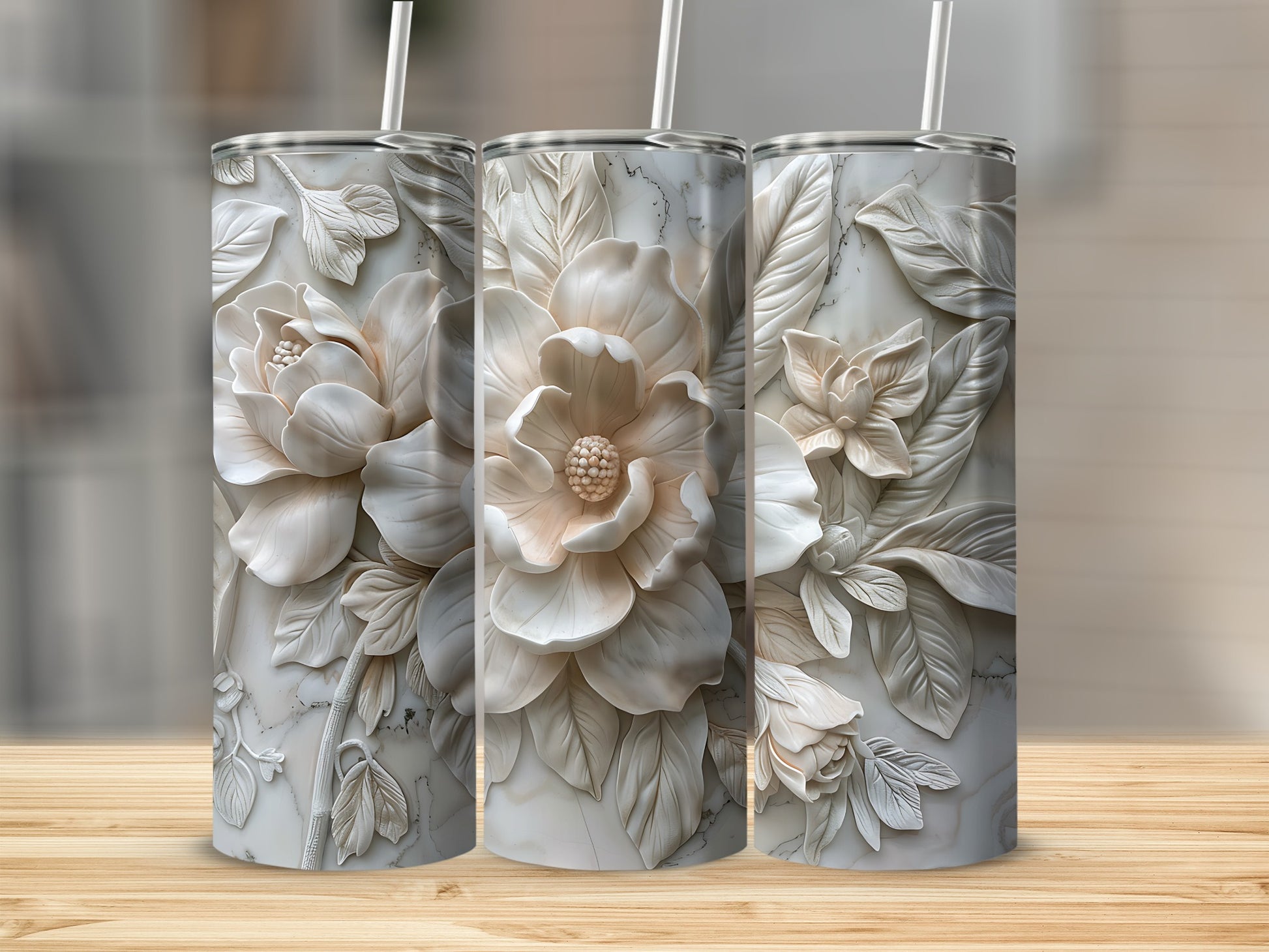 Three white floral embossed tumblers with straws on a wooden surface.