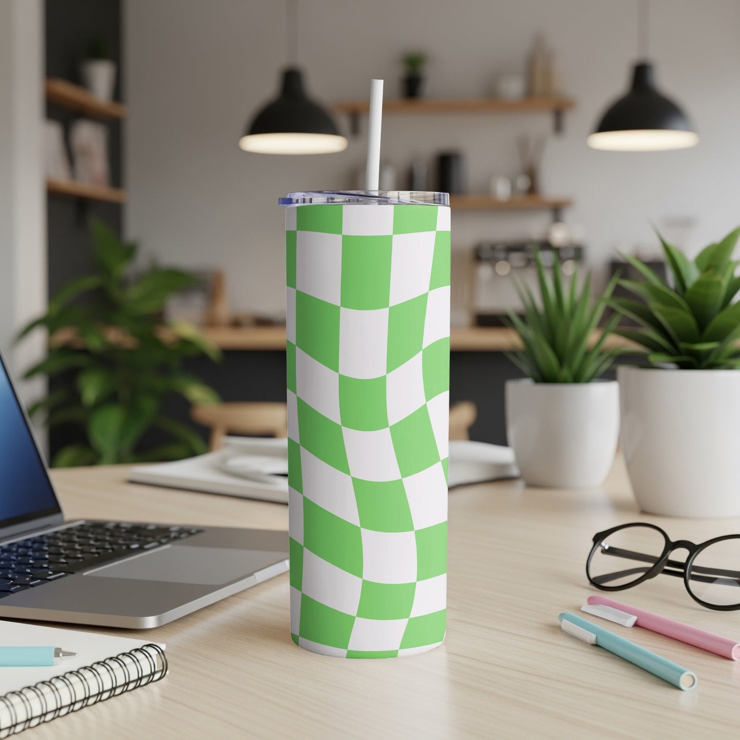 Green and white checkered tumbler with straw on a desk.