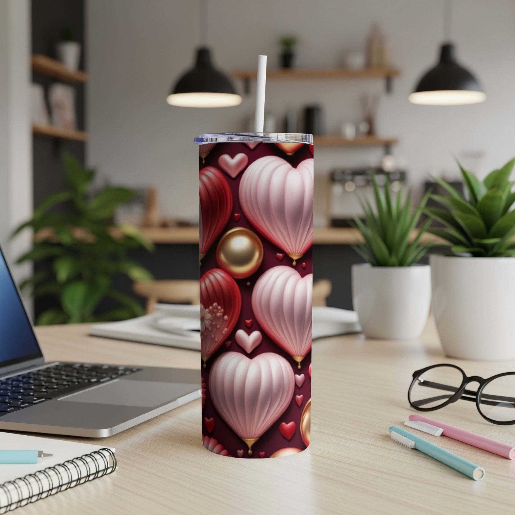 Red and pink heart-patterned tumbler with straw on a desk.