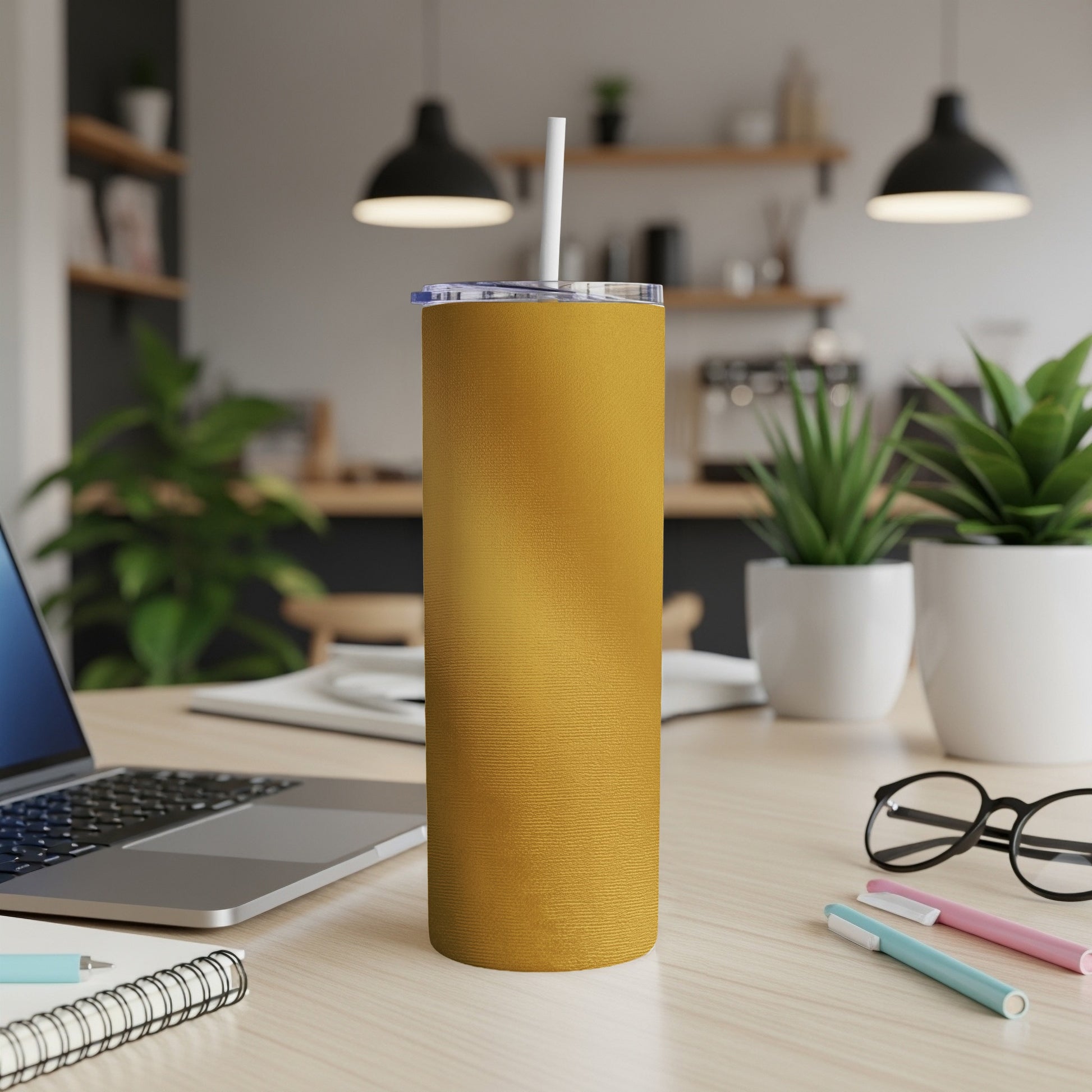 Yellow tumbler with a straw on a wooden desk next to a laptop.