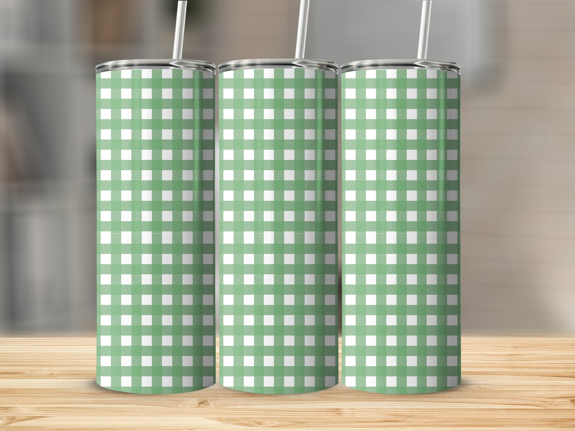 Three green and white checkered tumblers with straws on a wooden surface.