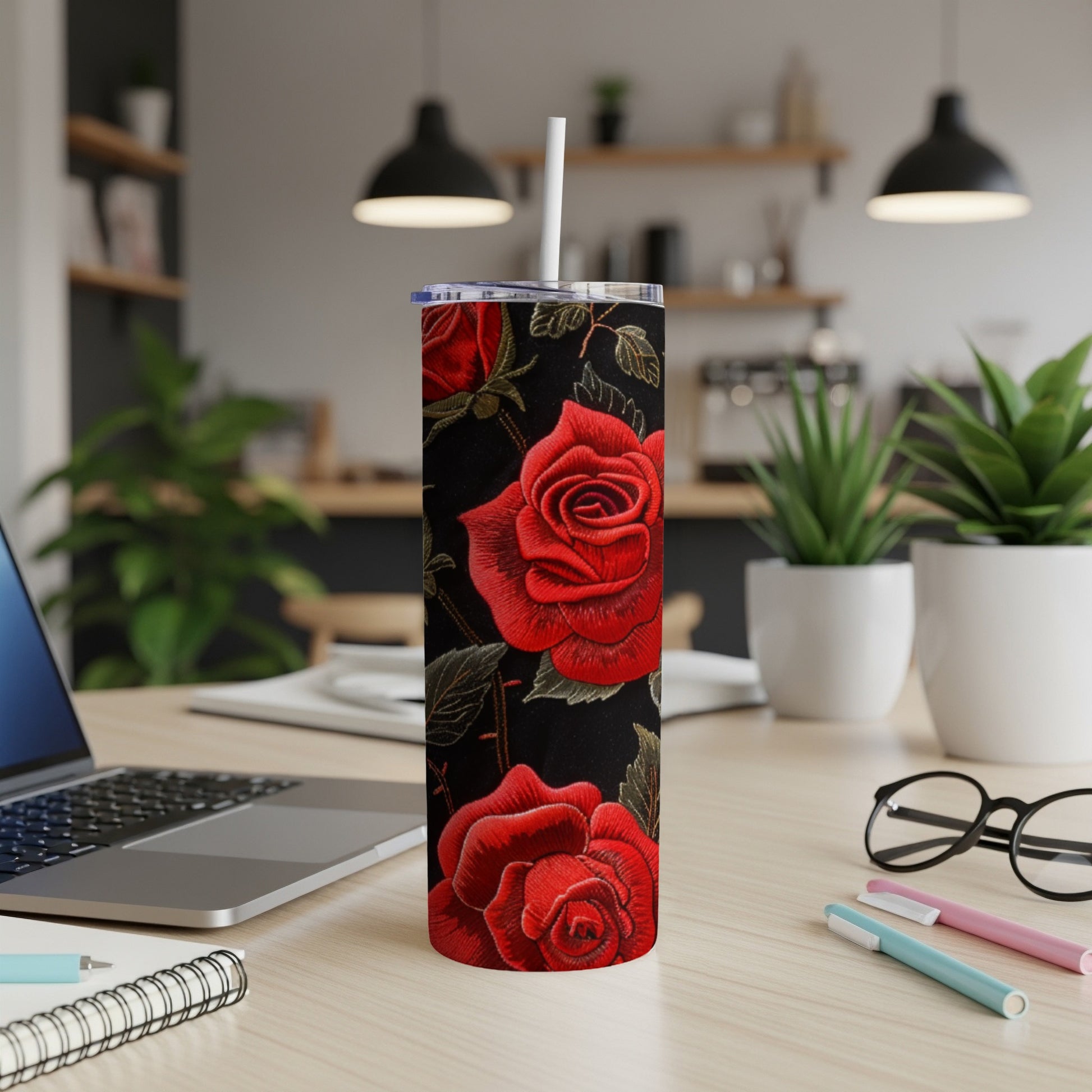 Black tumbler with embroidered red roses, featuring a straw and laptop in the background.