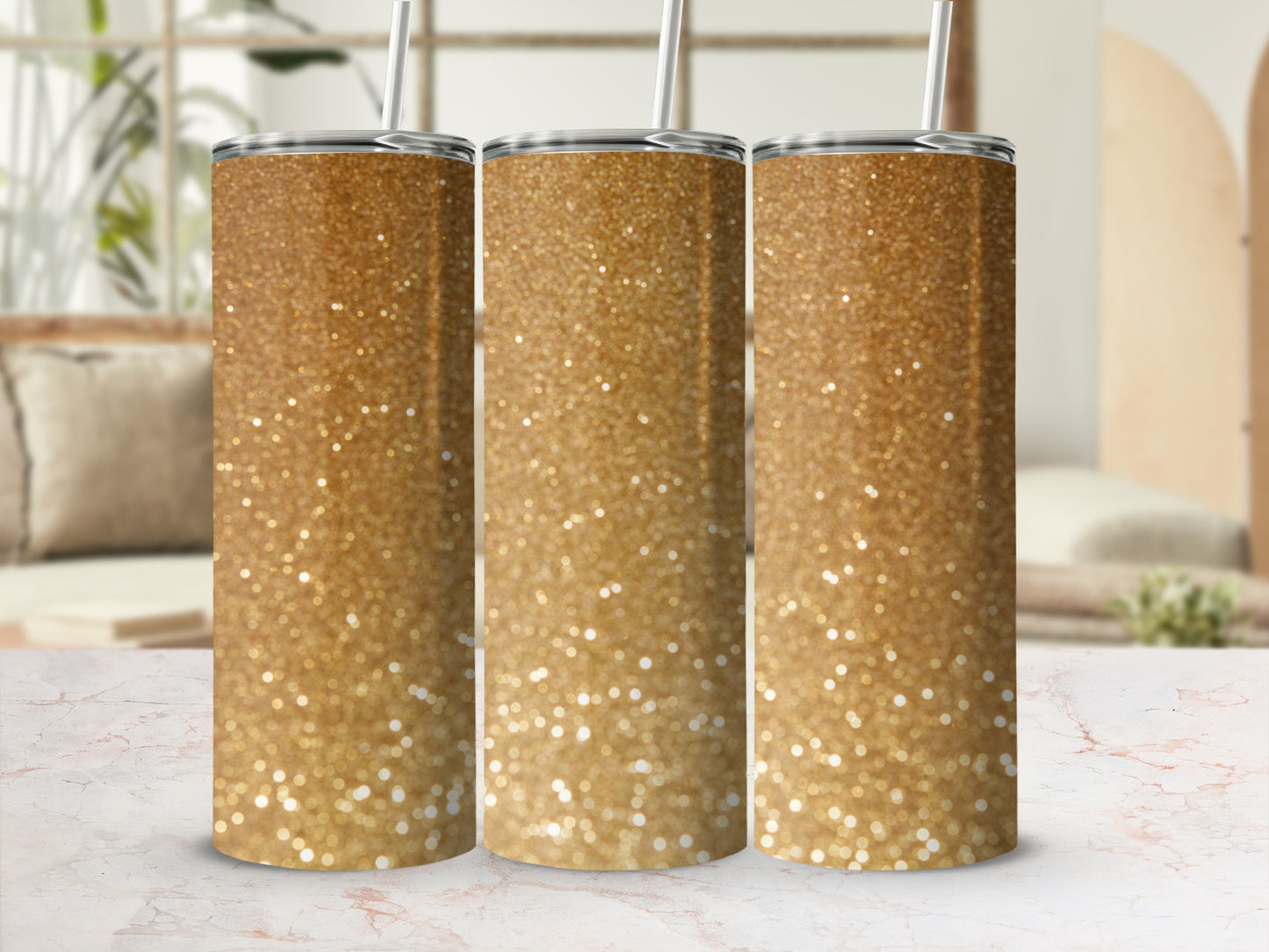 Three gold glitter tumblers with straws arranged on a marble surface.