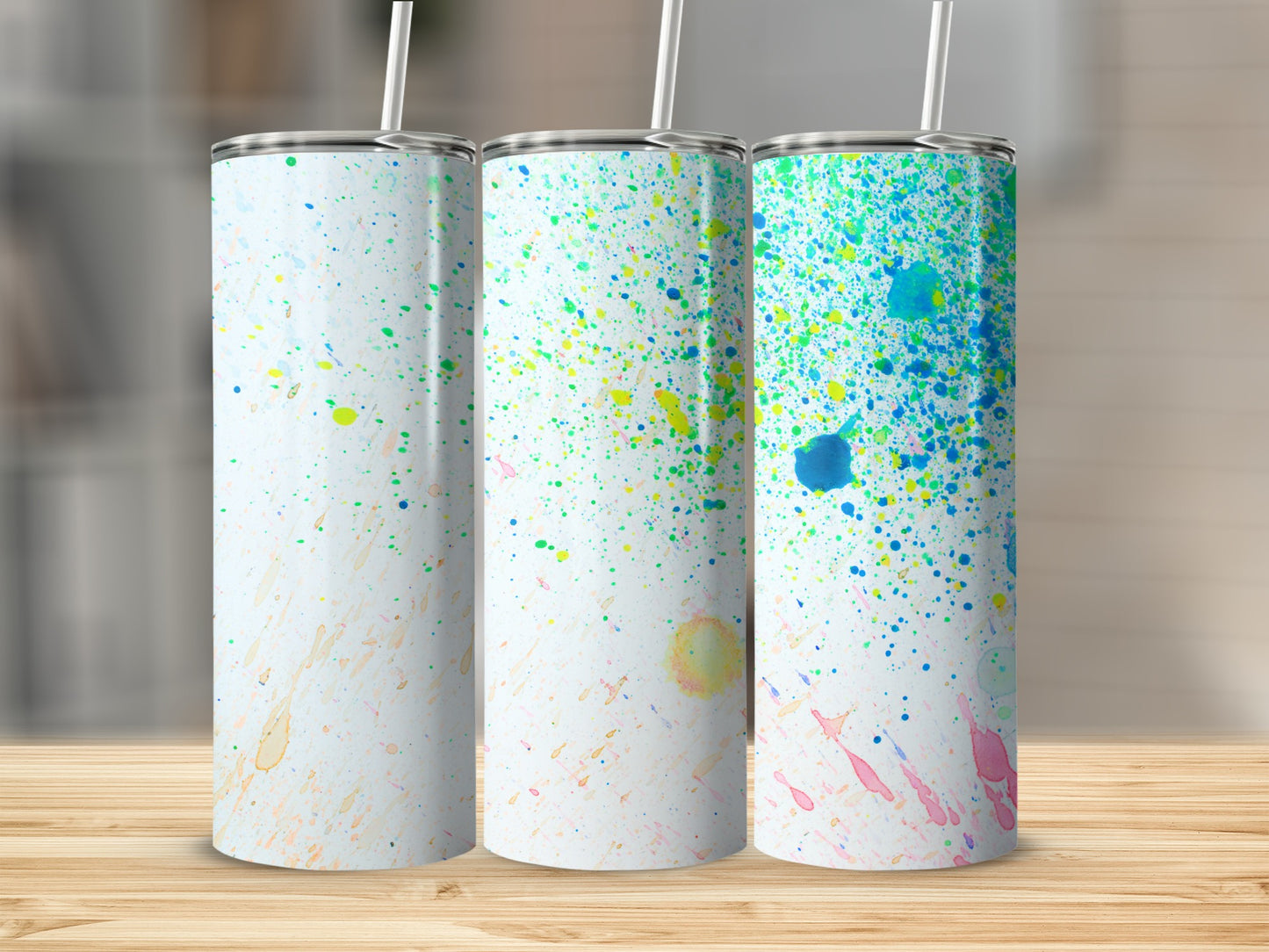 Three white tumblers with colorful paint splatters, arranged on a wooden surface.