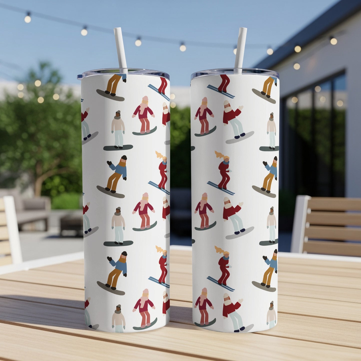 Two insulated tumblers with a repeating pattern of cartoon snowboarders on a wooden table.