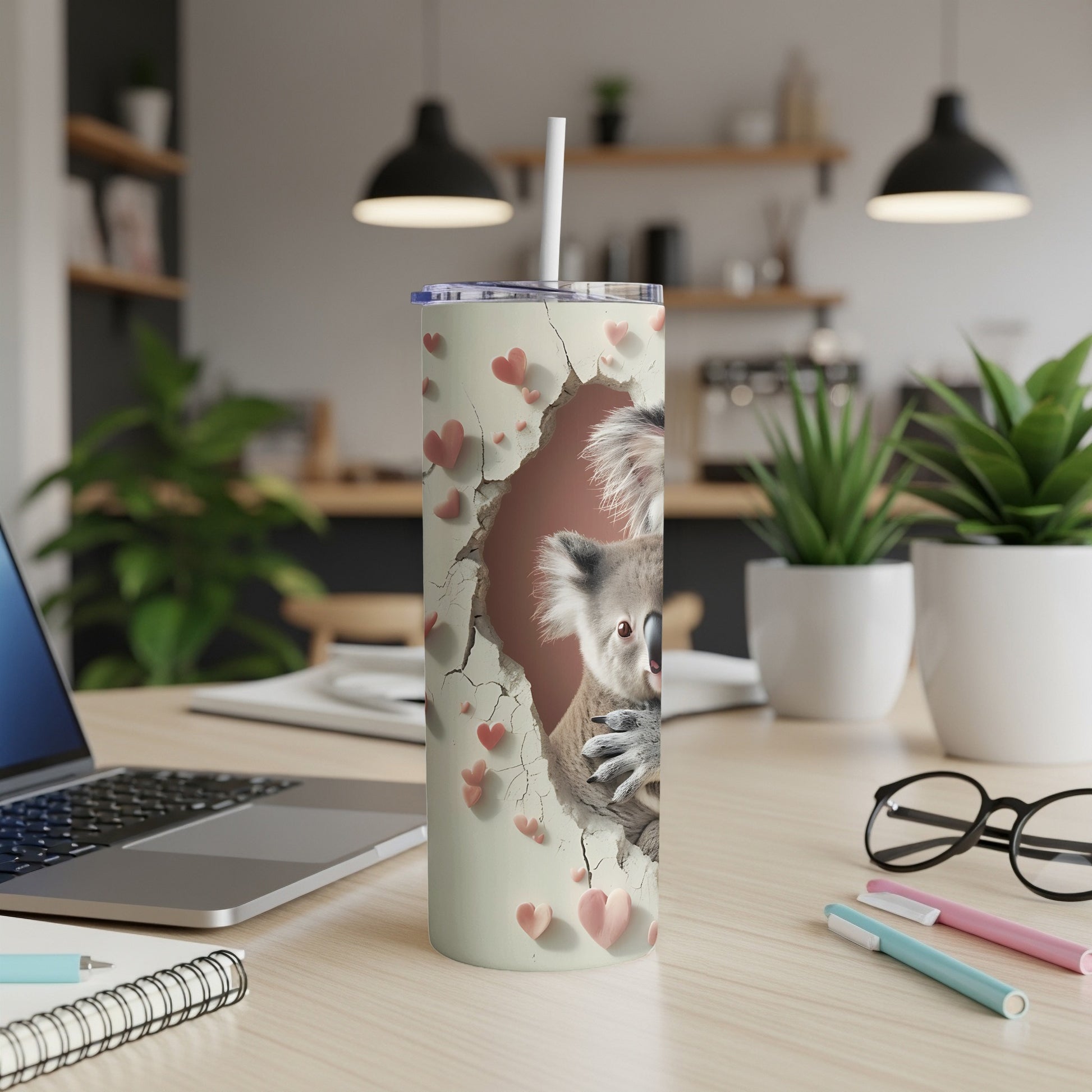 White tumbler with a koala and hearts design, resting on a desk.
