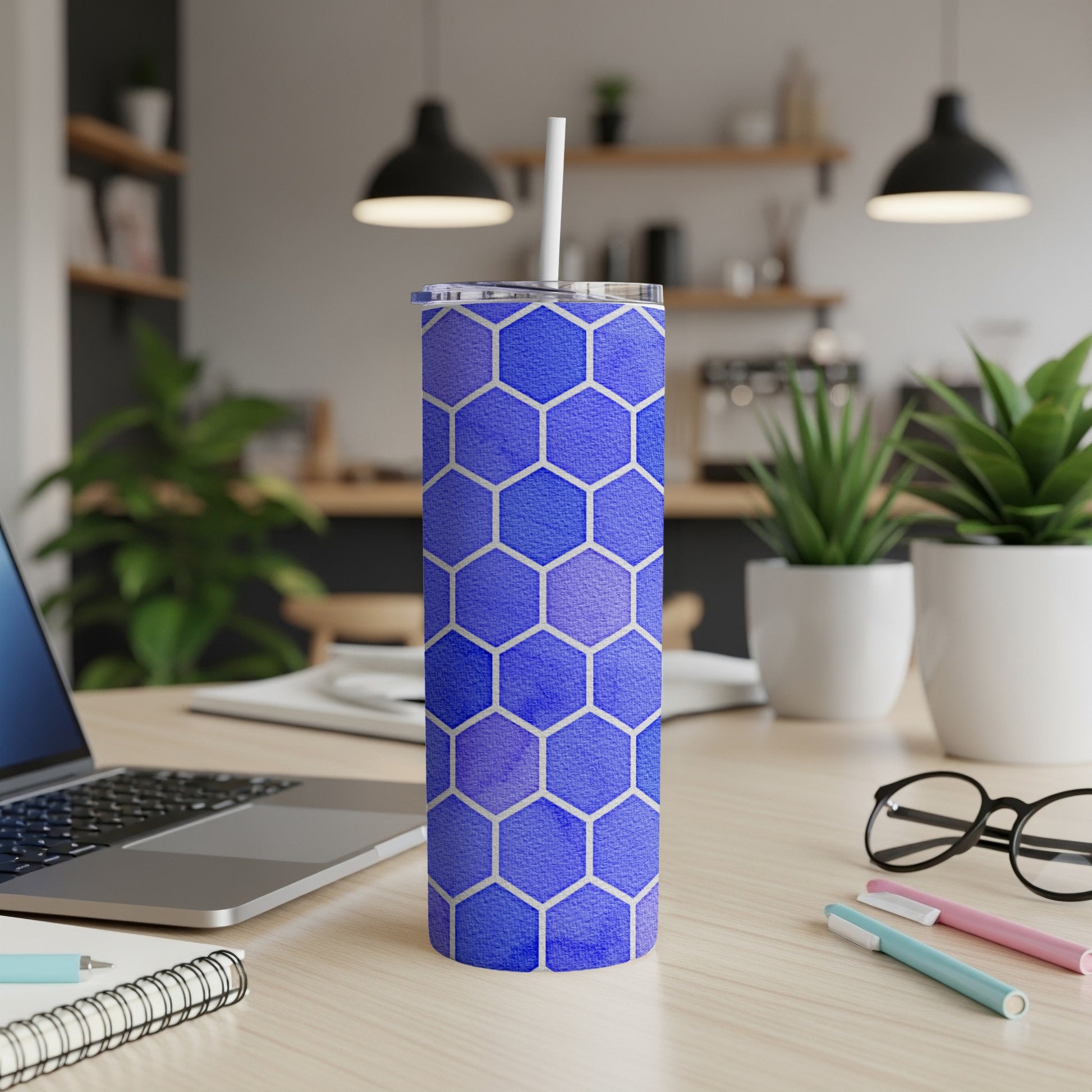 Blue tumbler with white hexagon pattern and straw, on a desk.