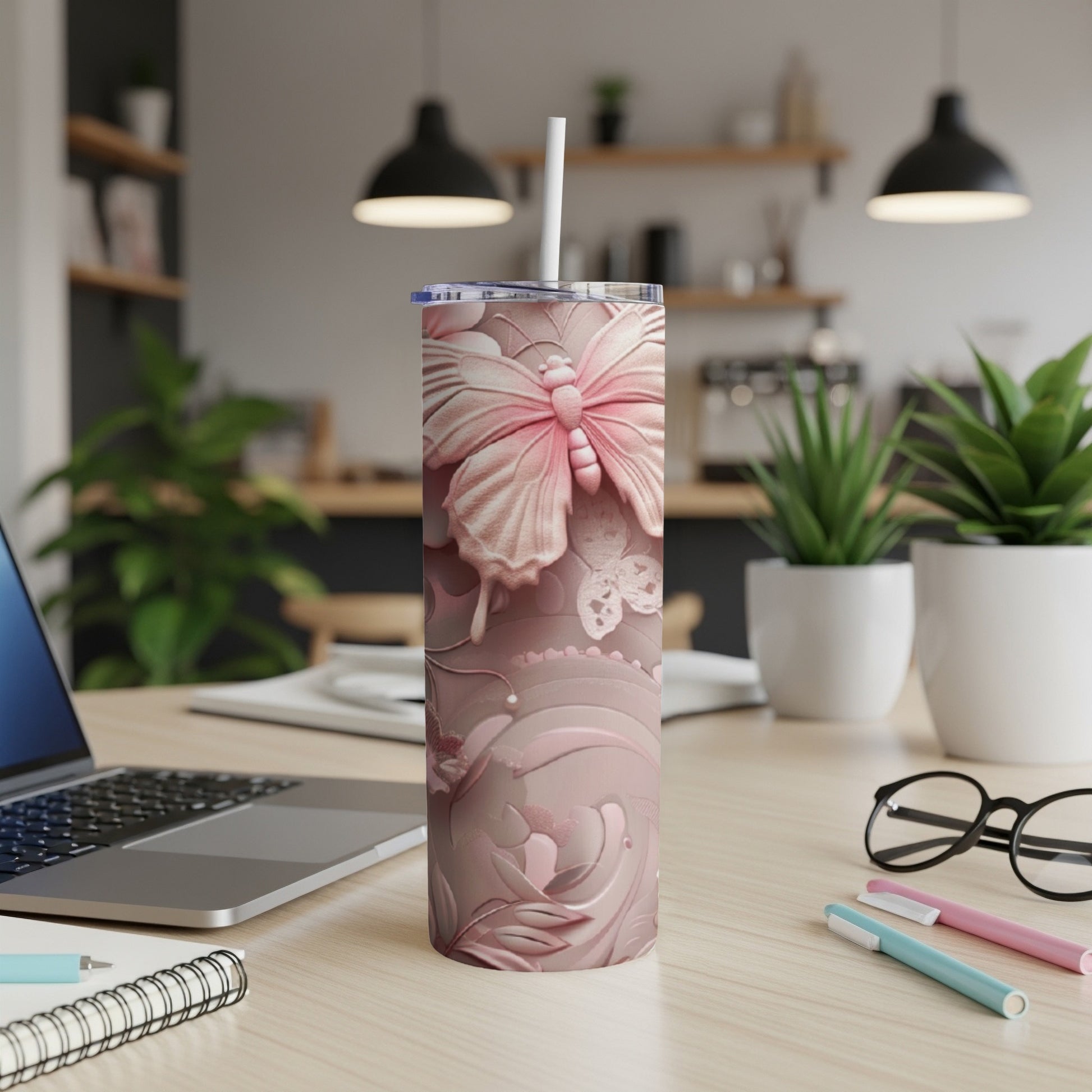 Pink butterfly tumbler with straw on desk with laptop and pens.