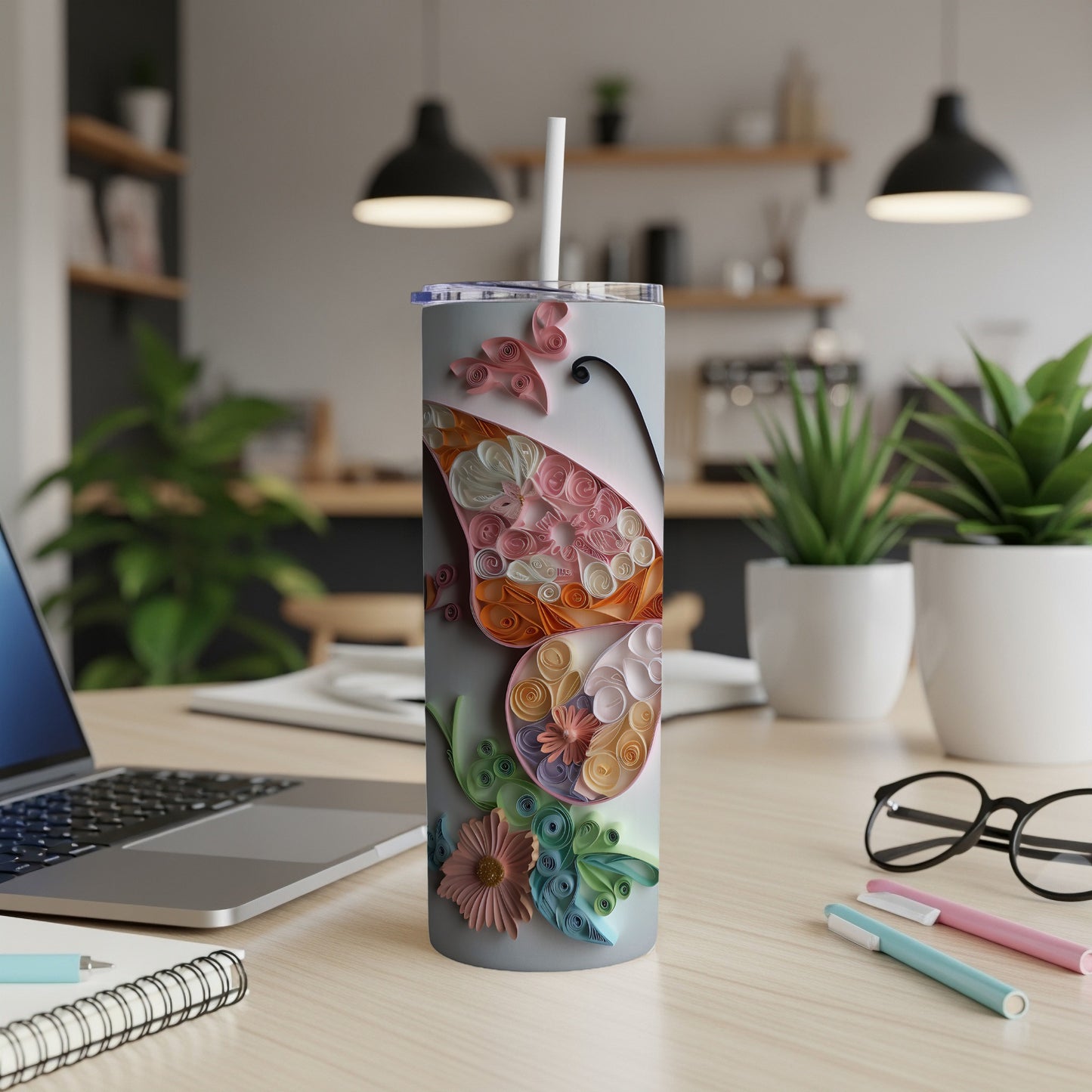 Tumbler with quilled butterfly and floral design on a desk with laptop and glasses.