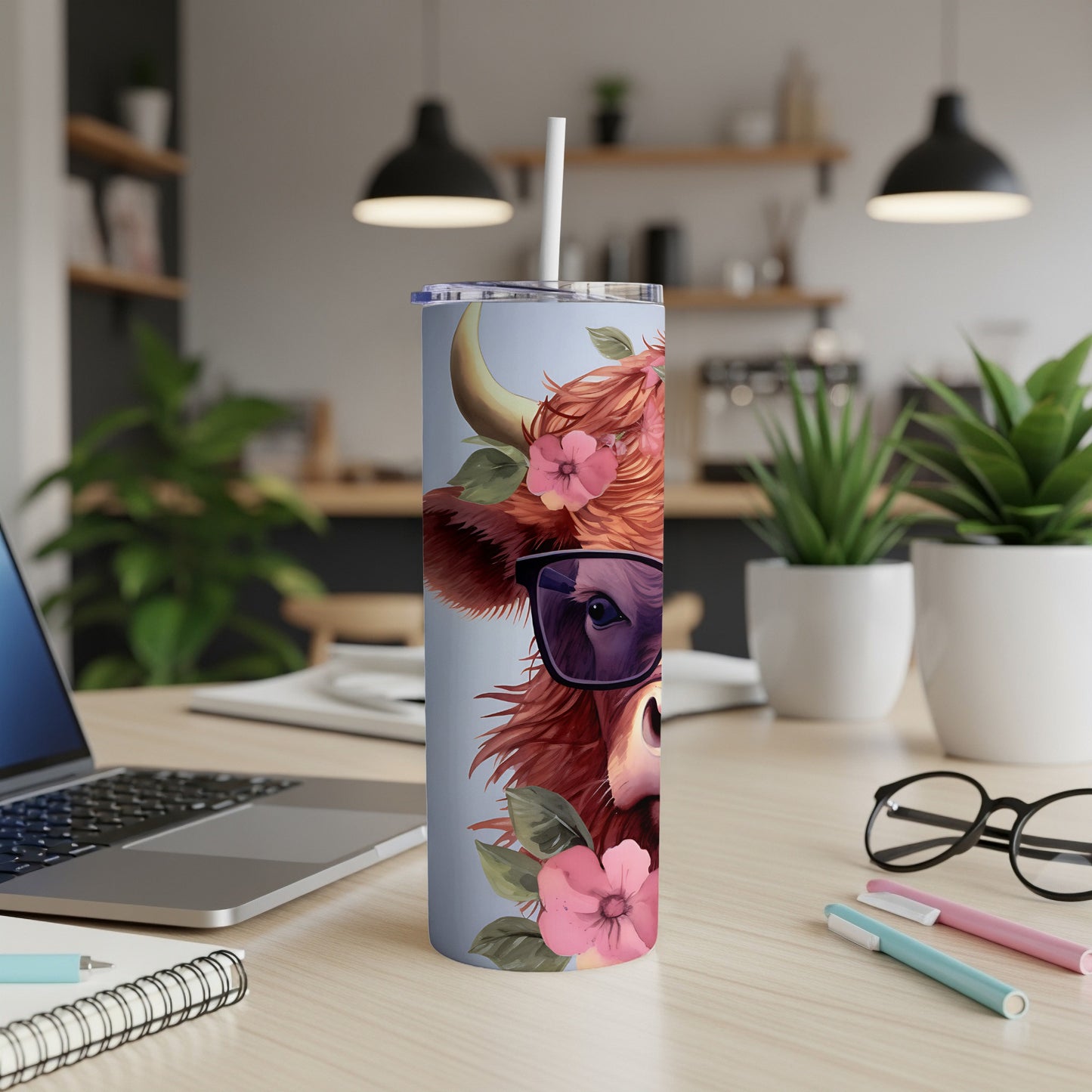 Cow with sunglasses and flowers on a tumbler with a laptop and pens.