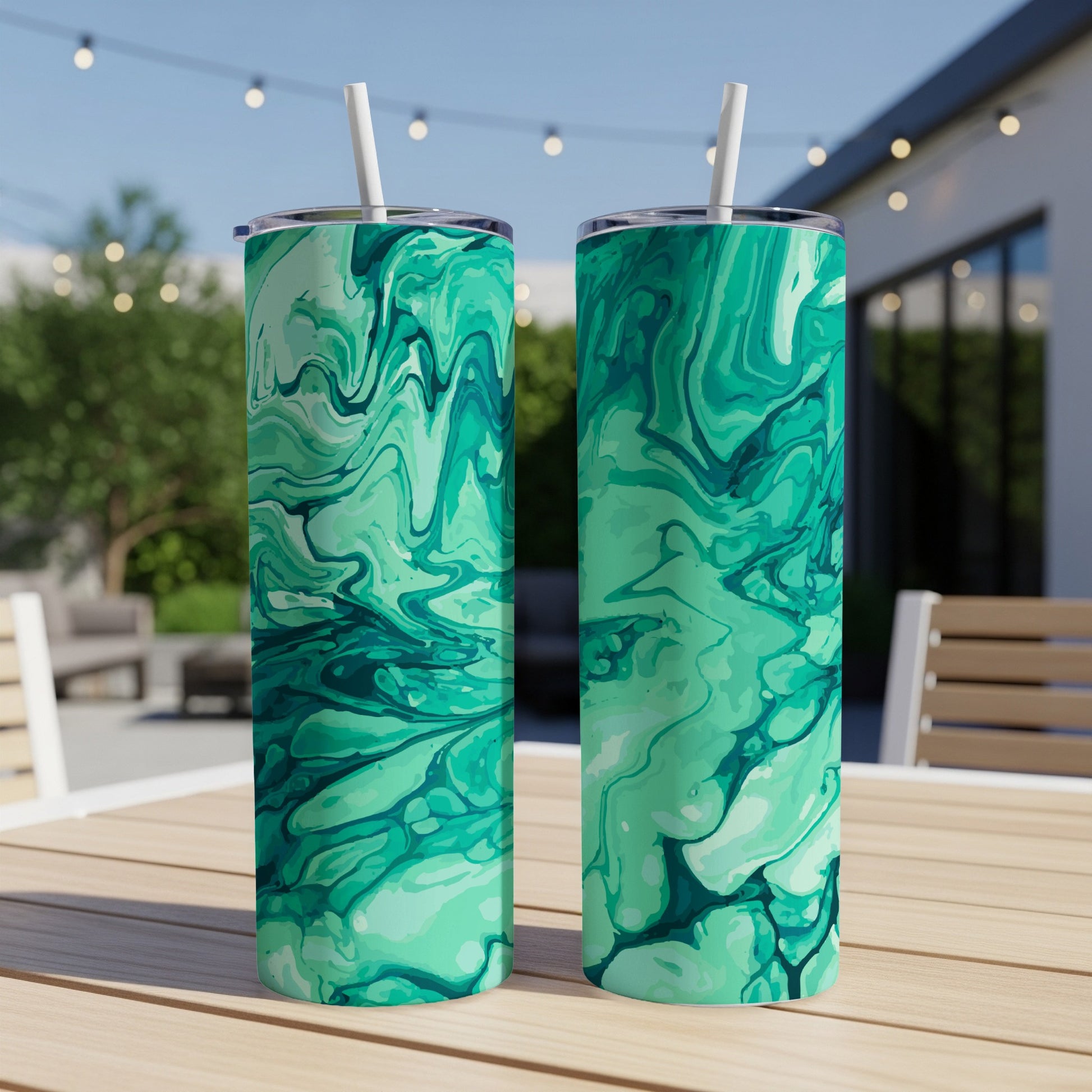 Two green marble design tumblers with white straws on a wooden table, outdoors.