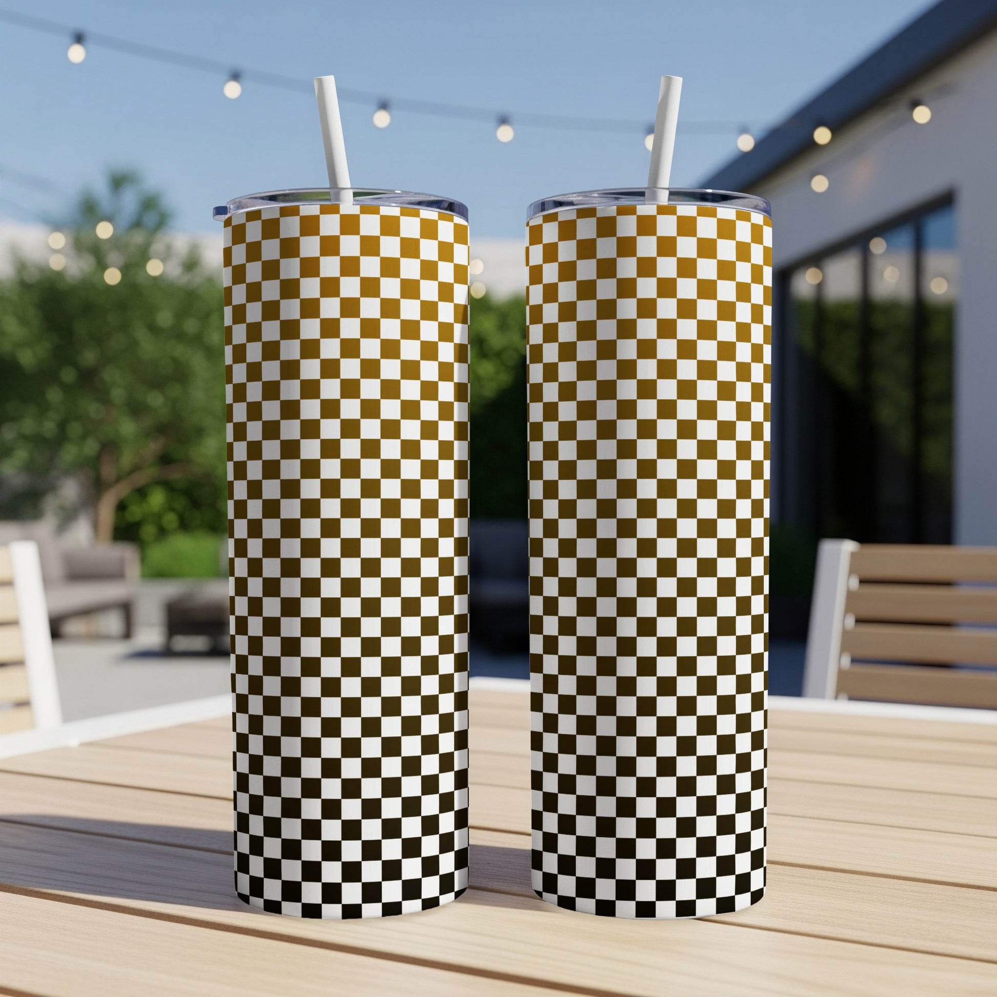 Two tall tumblers with a checkered pattern sit on a wooden table outdoors.