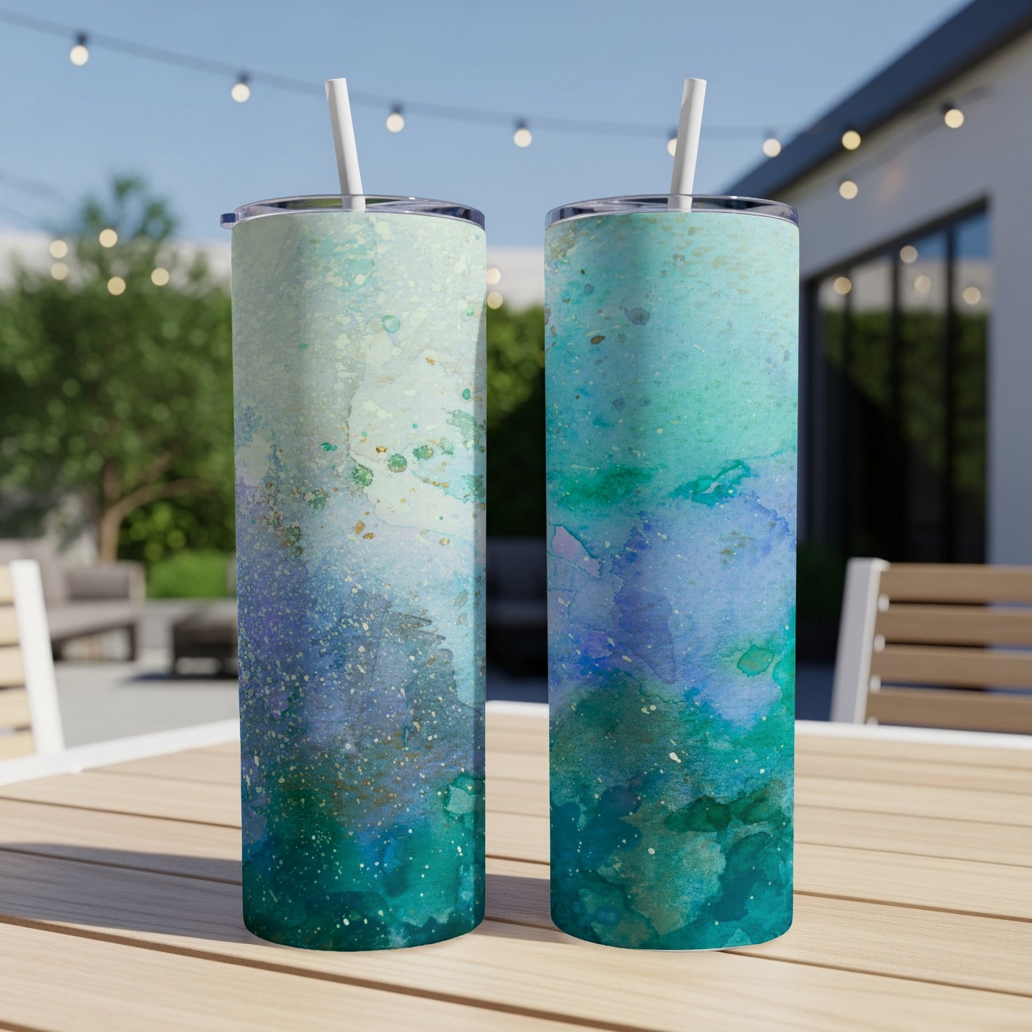 Two tumblers with blue and green watercolor abstract designs sit on a wooden table.
