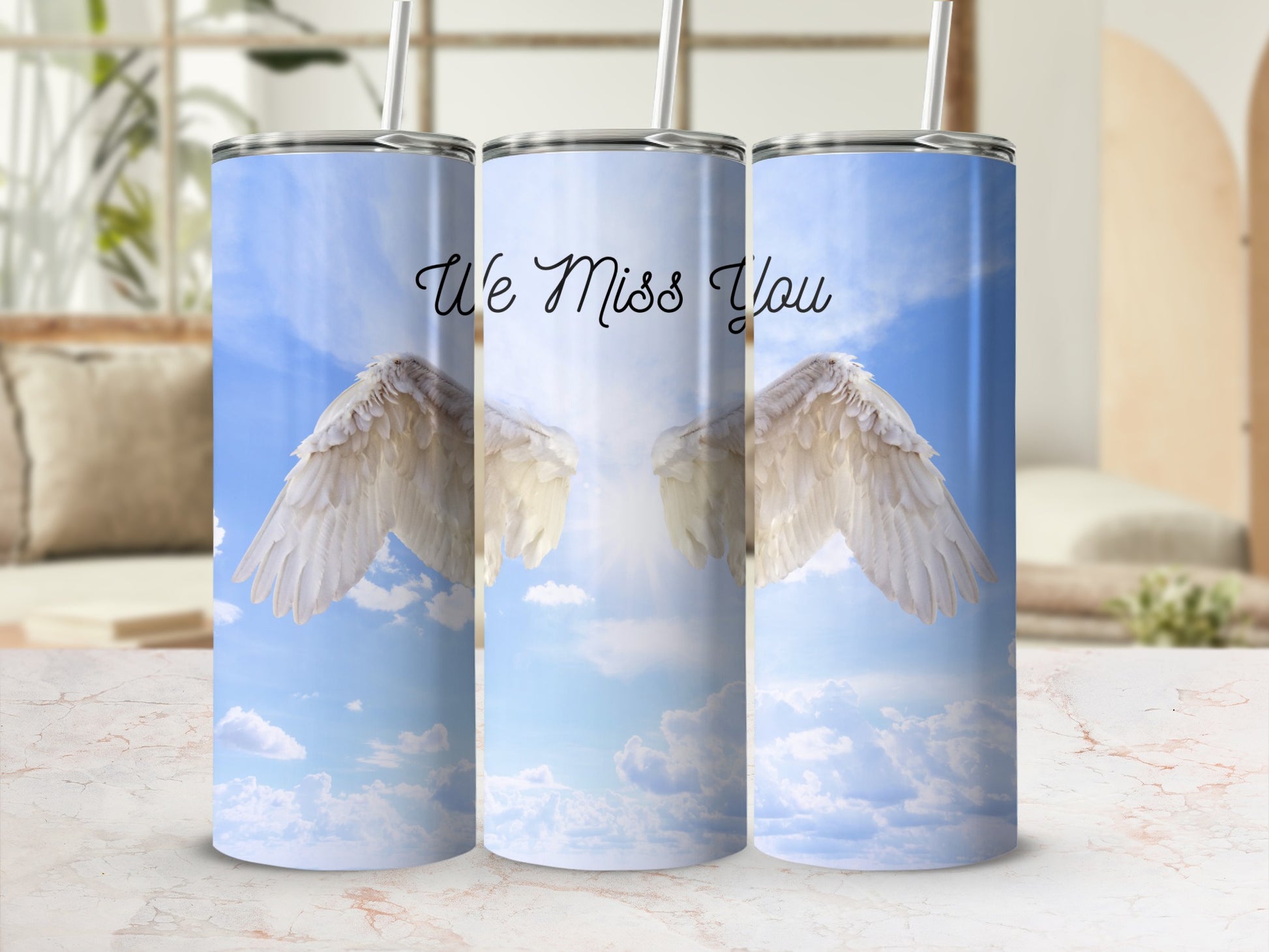 Angel wings and "We Miss You" text on a tumbler against a cloudy sky background.