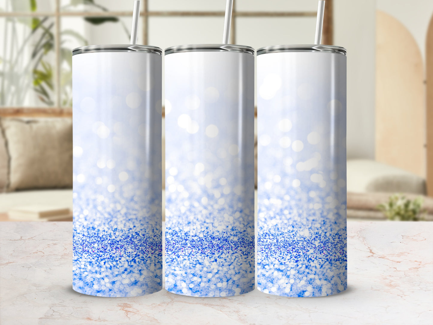 Three white tumblers with blue glitter gradient and straw on marble countertop.