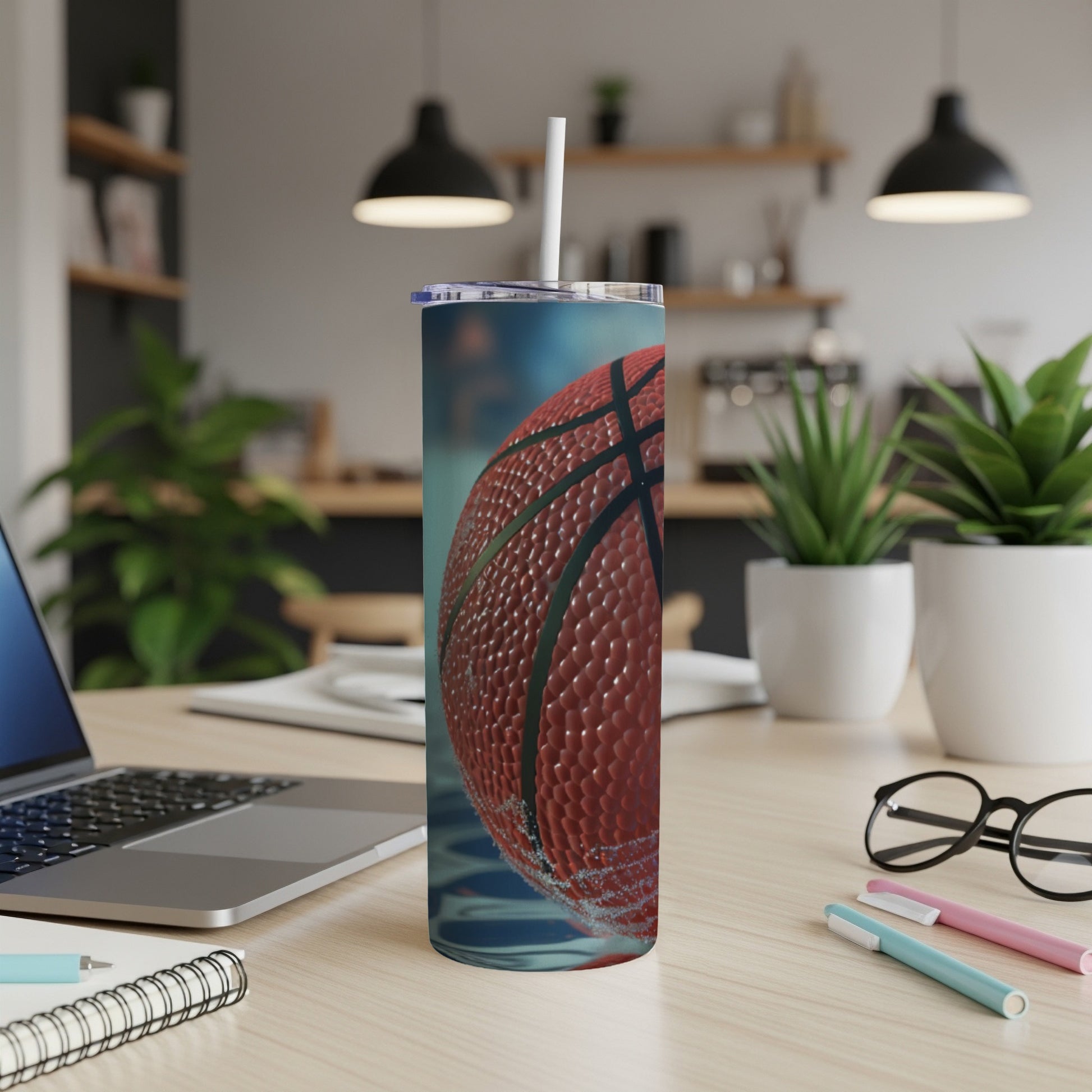 Basketball tumbler with straw on a desk with a laptop and pens.