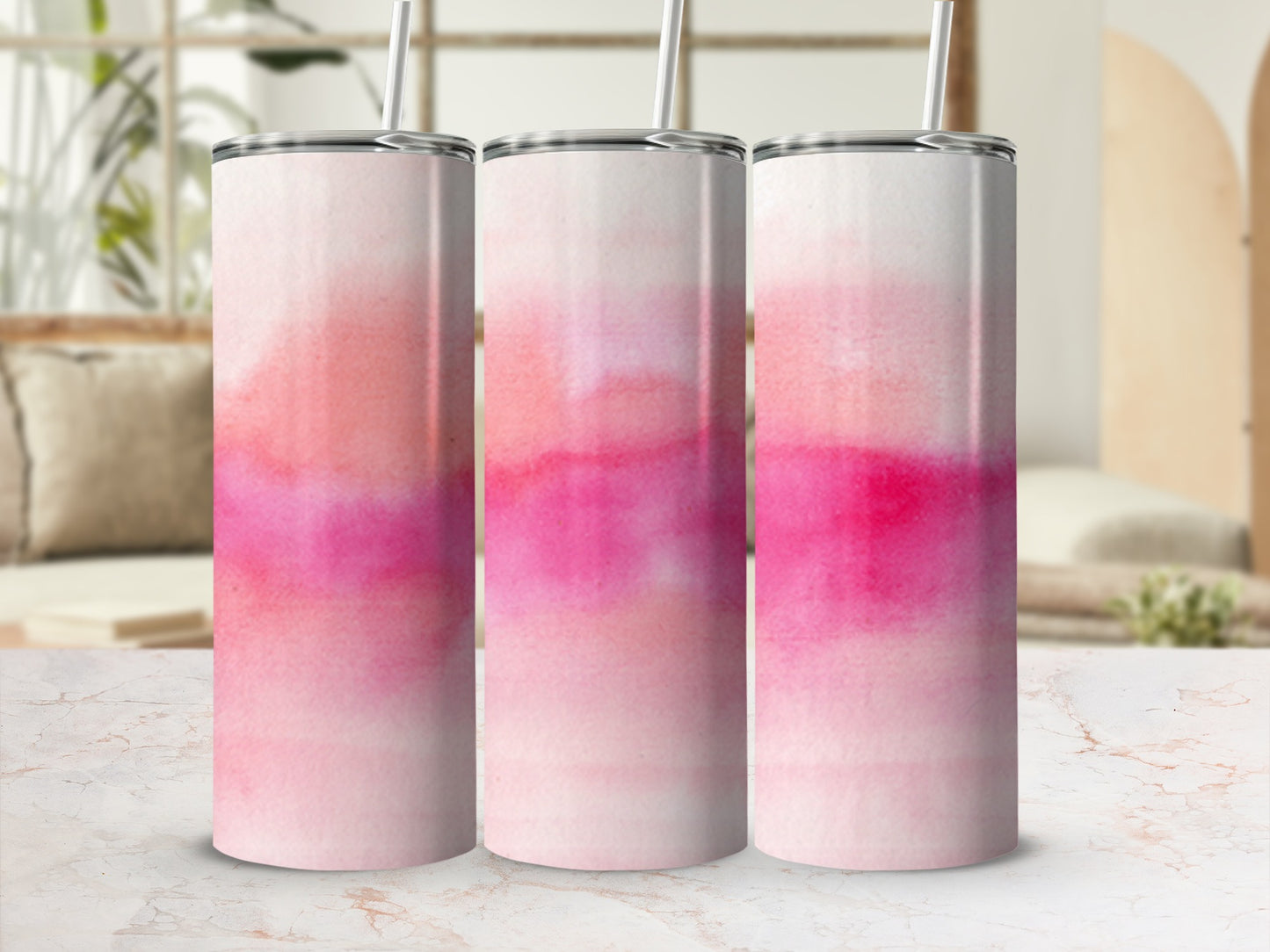 Three pink watercolor abstract pattern tumblers with straws on a marbled surface.