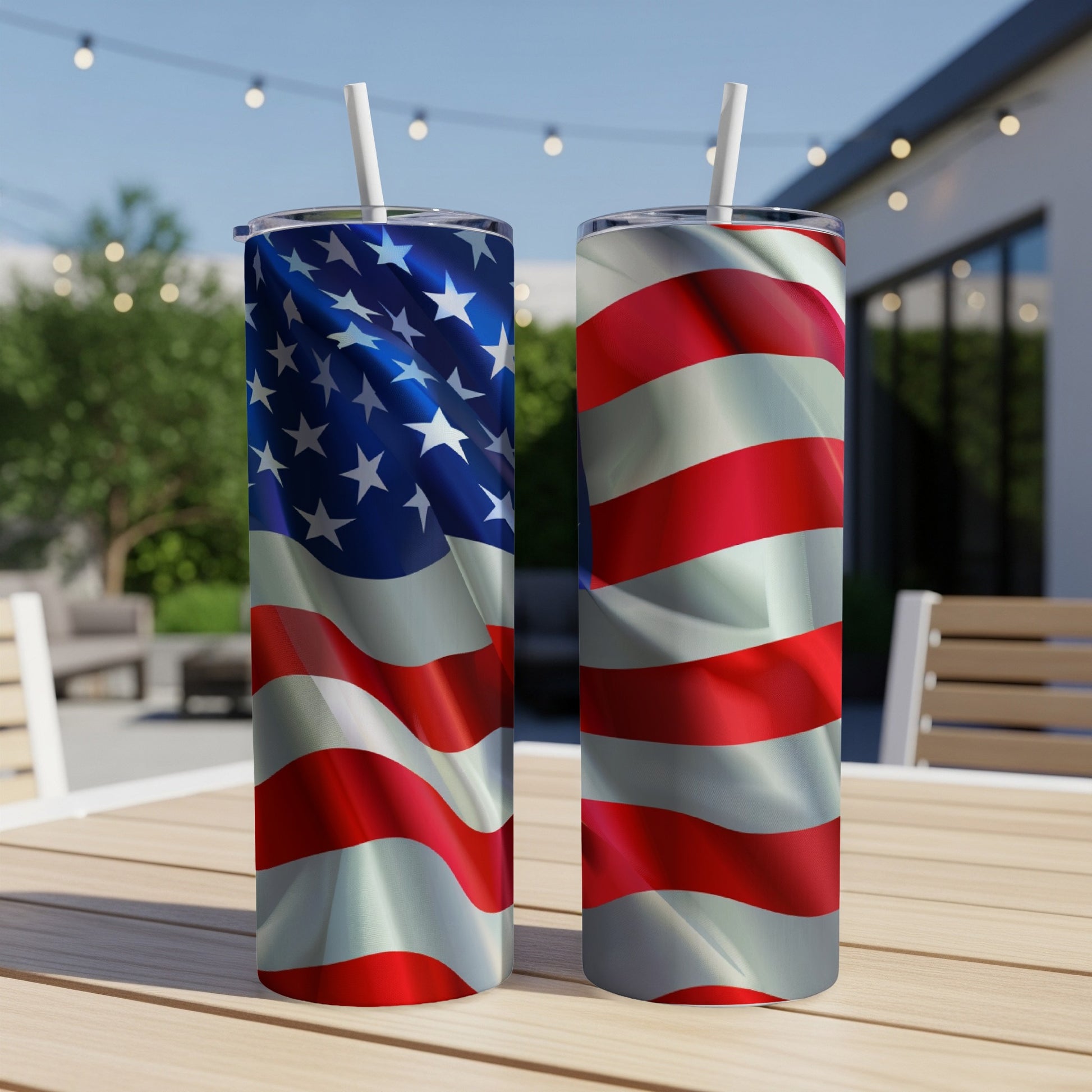 Two American flag tumblers with straws on a wooden table outdoors.