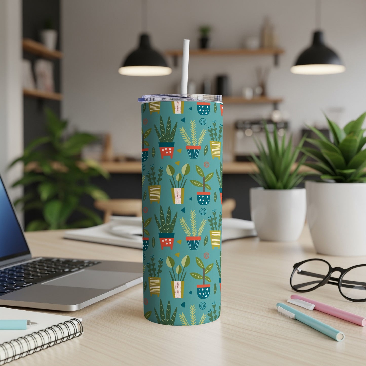 Teal tumbler with potted plant pattern and white straw, on a desk.