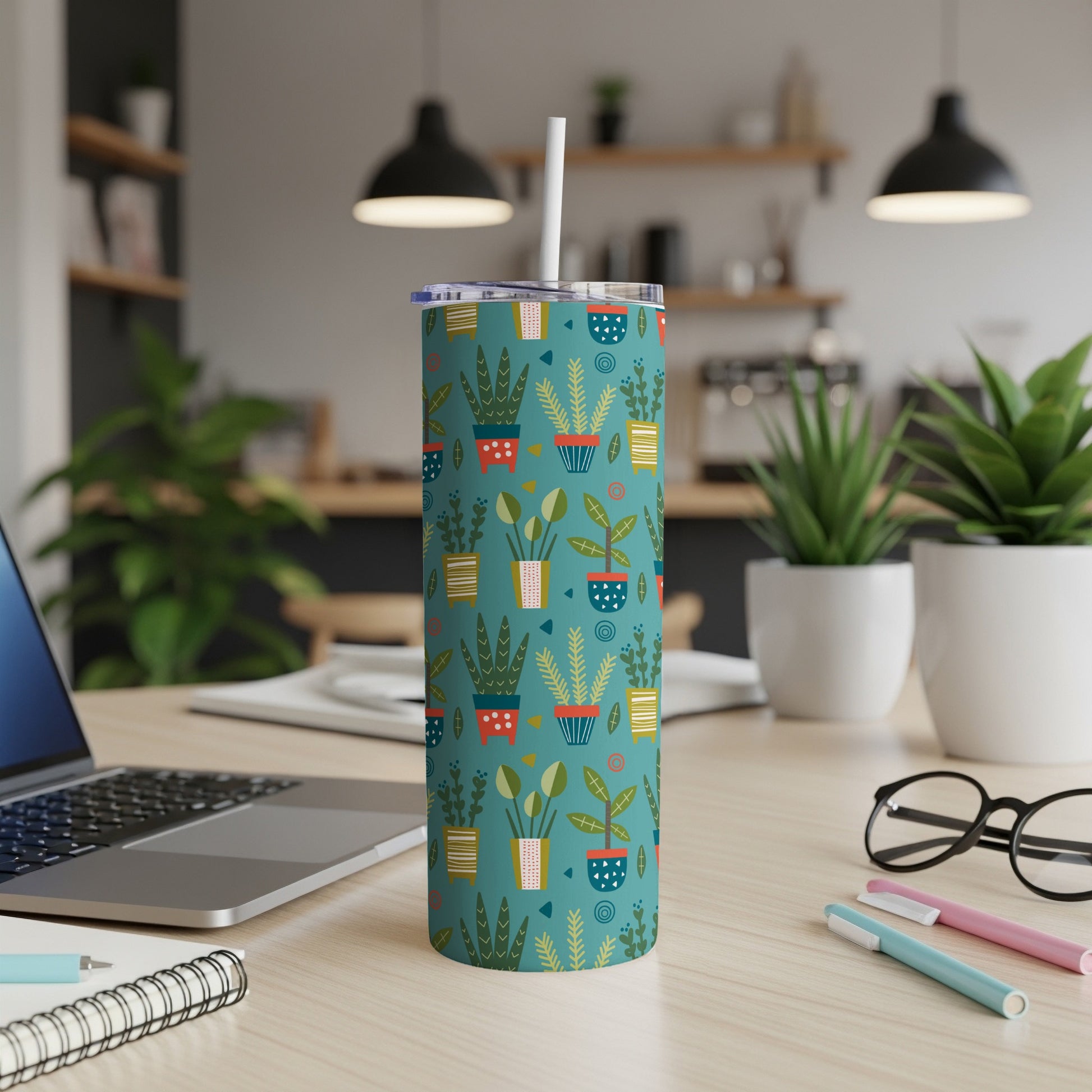Teal tumbler with potted plant pattern and white straw, on a desk.