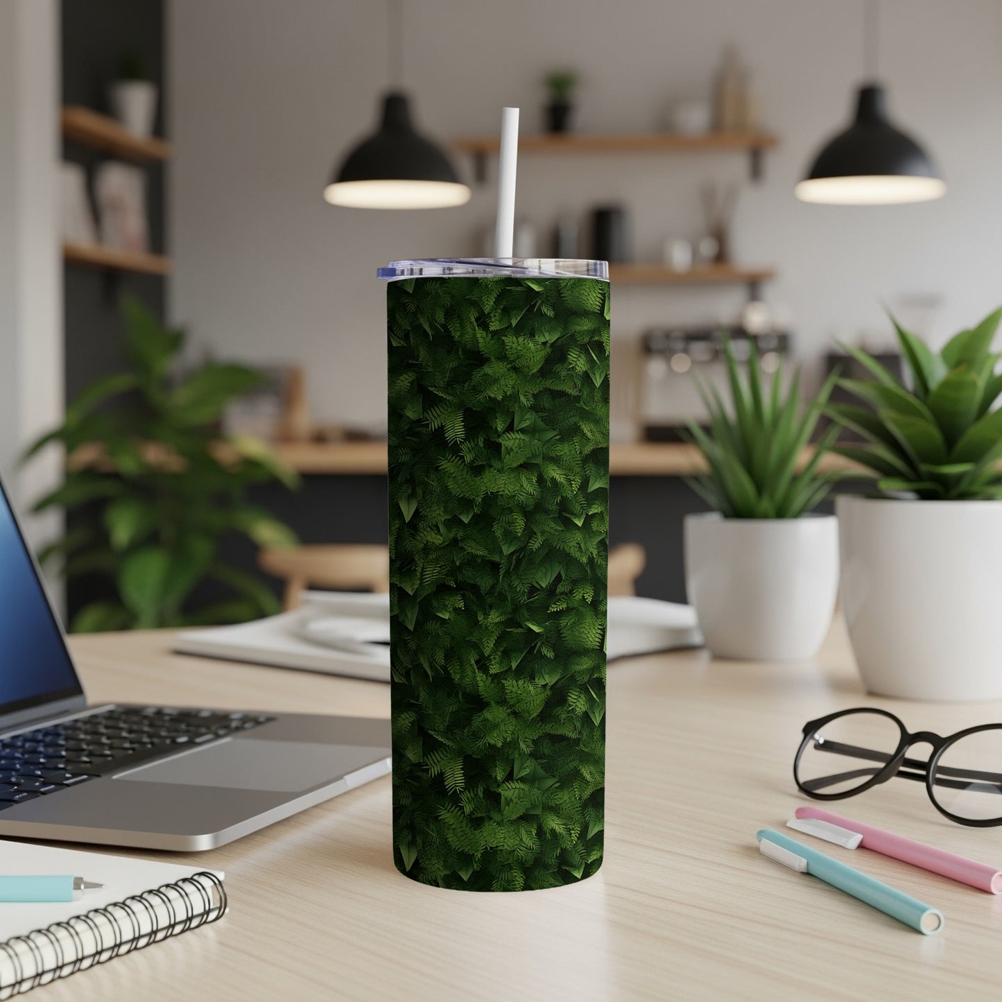 Green fern pattern tumbler with straw on a desk with a laptop and pens.