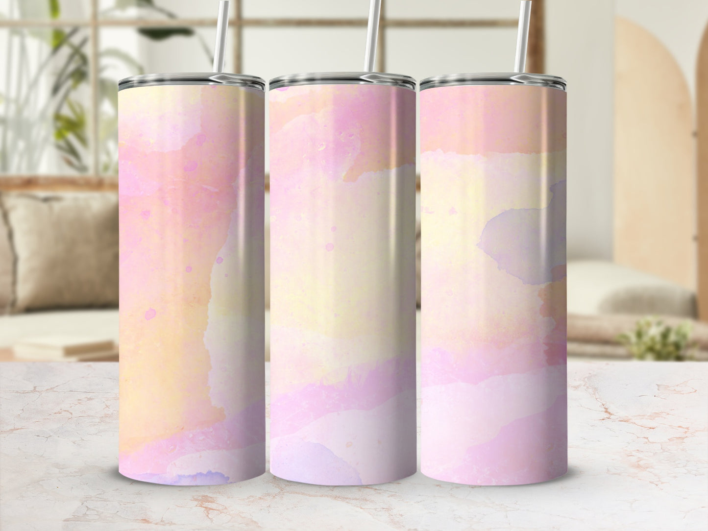 Three pastel watercolor tumblers with straws on a marble surface.