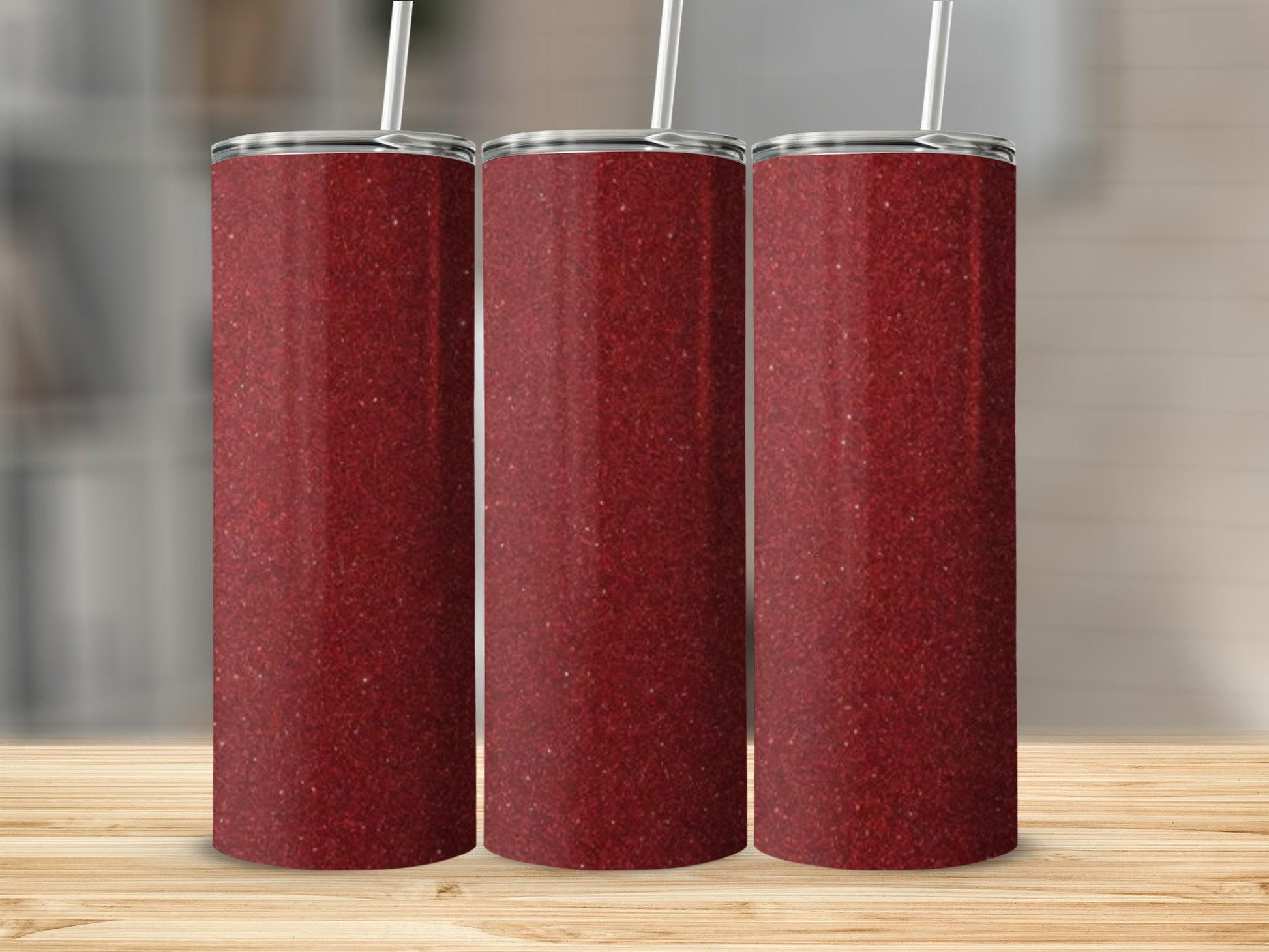 Three glittery red tumblers with straws stand on a wooden surface.