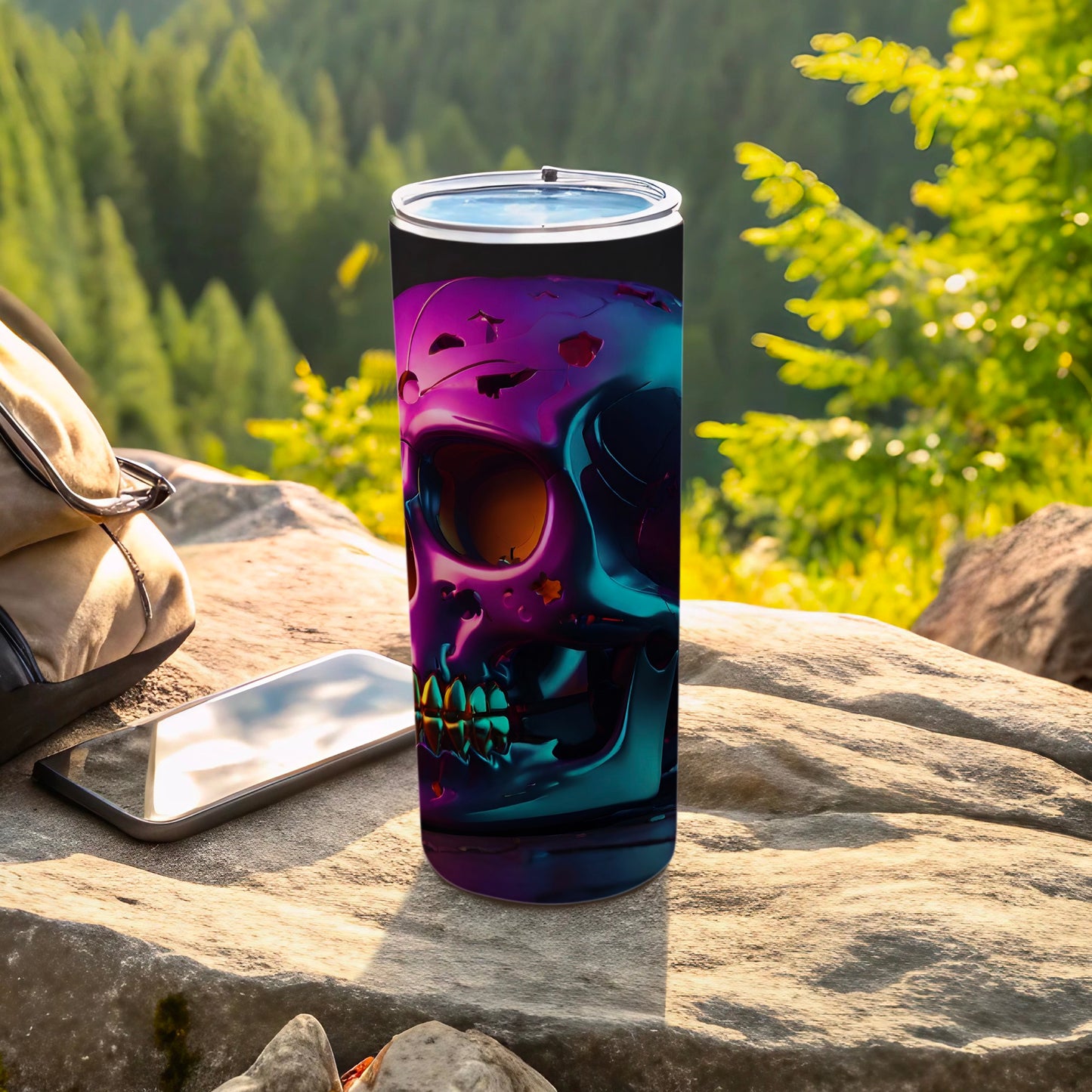 Iridescent skull tumbler on rock next to phone and backpack.