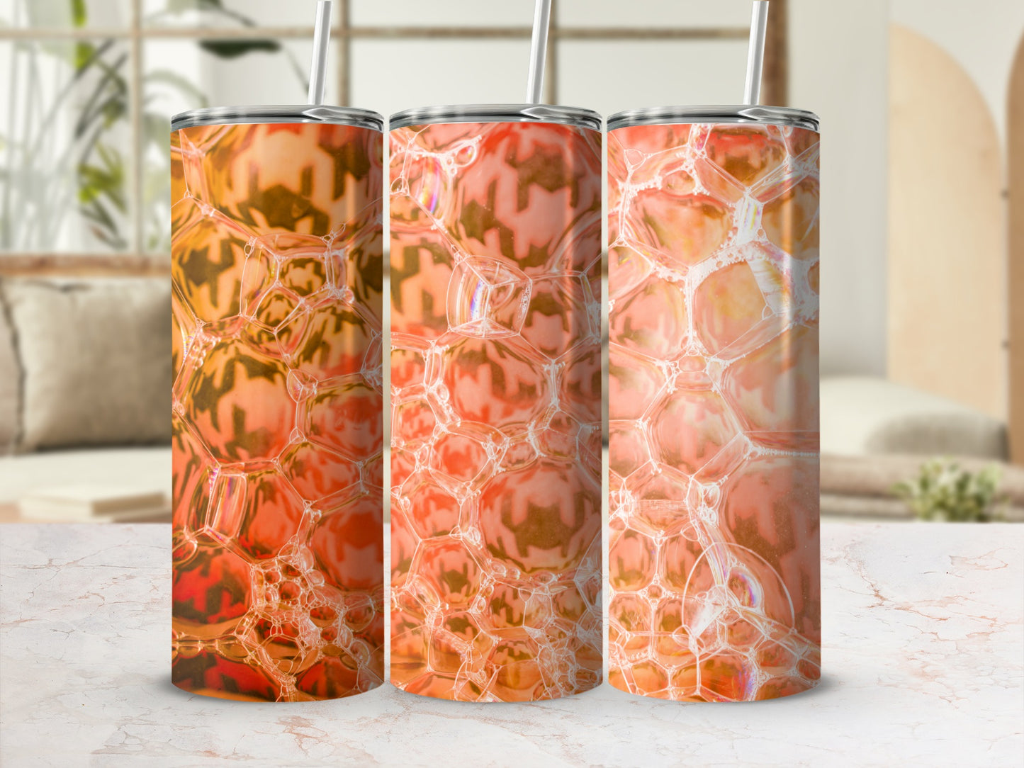 Three orange bubble pattern tumblers with straws on a marble surface.