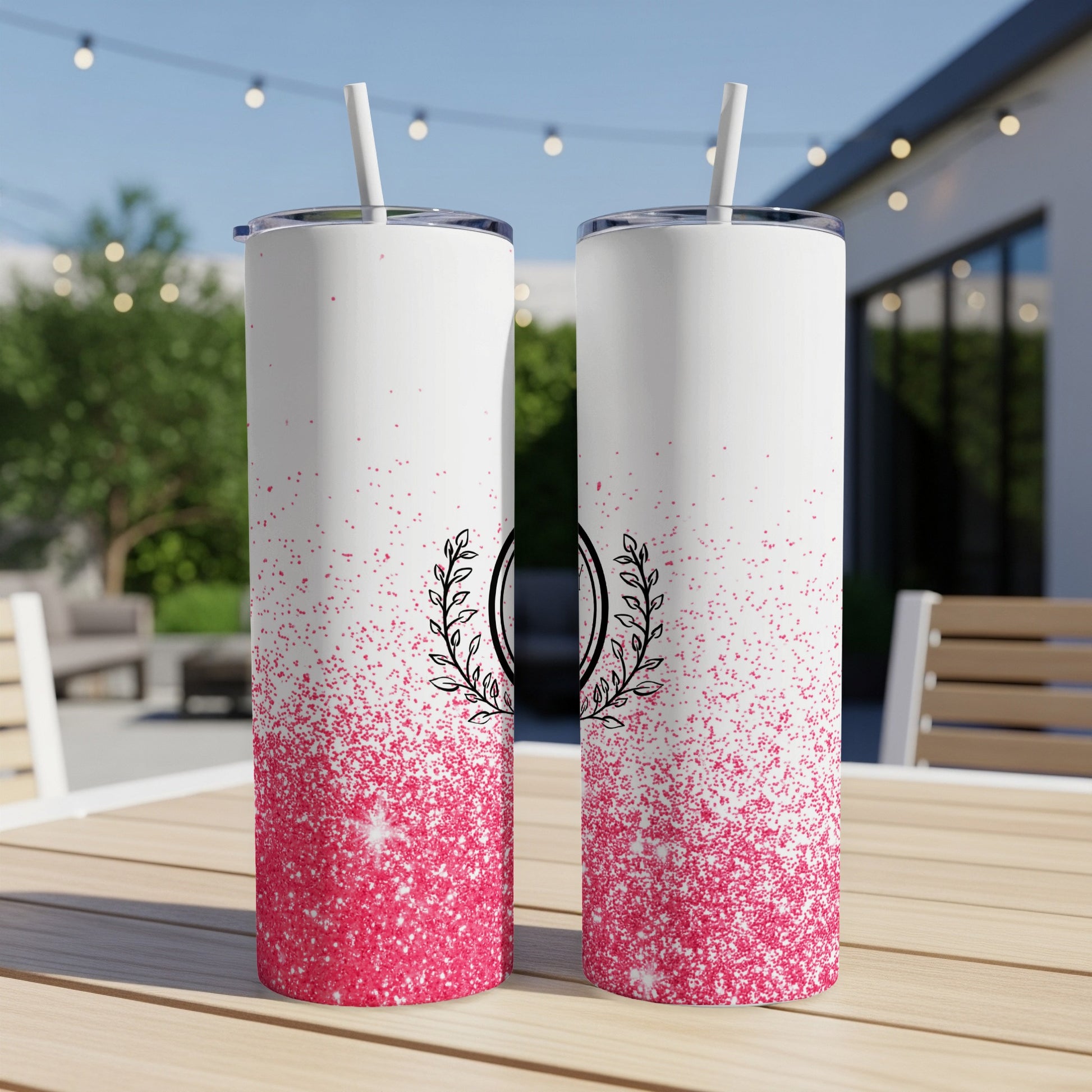 Two white tumblers with pink glitter and floral wreath designs sit on a table.