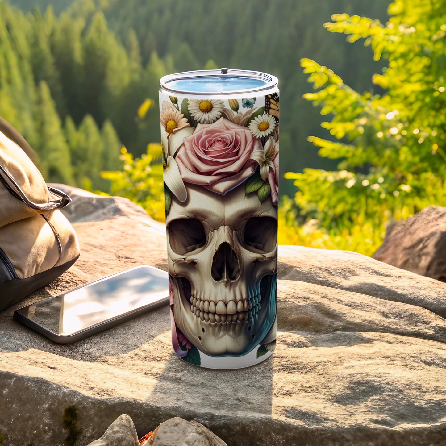Tumbler with skull adorned with flowers and butterflies, placed on rock.