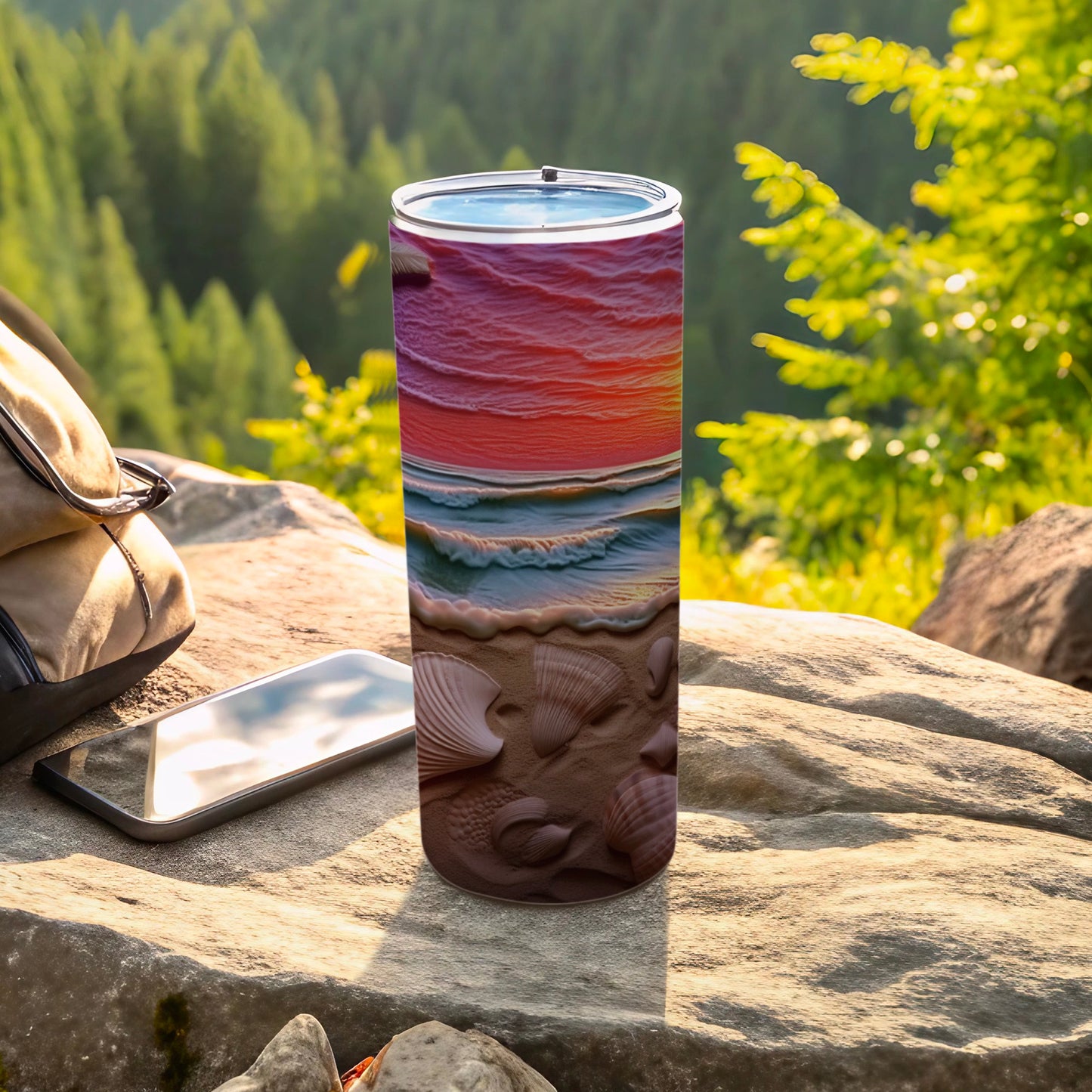 Tumbler with seashell and ocean sunset design, resting on rocks.