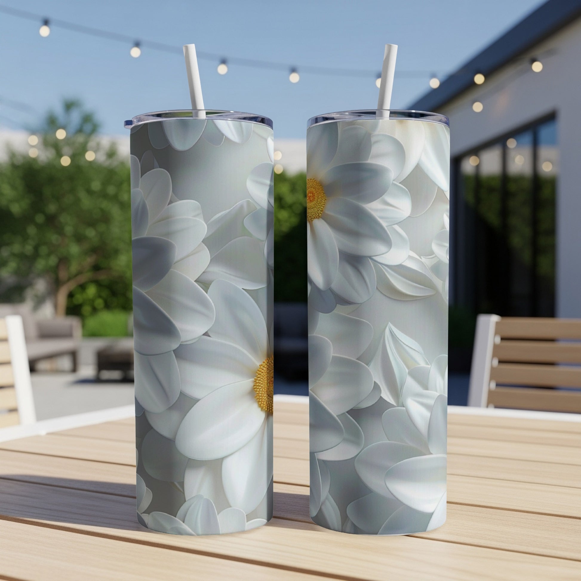Two tumblers with a white floral design featuring yellow centers, on a wooden table outdoors.
