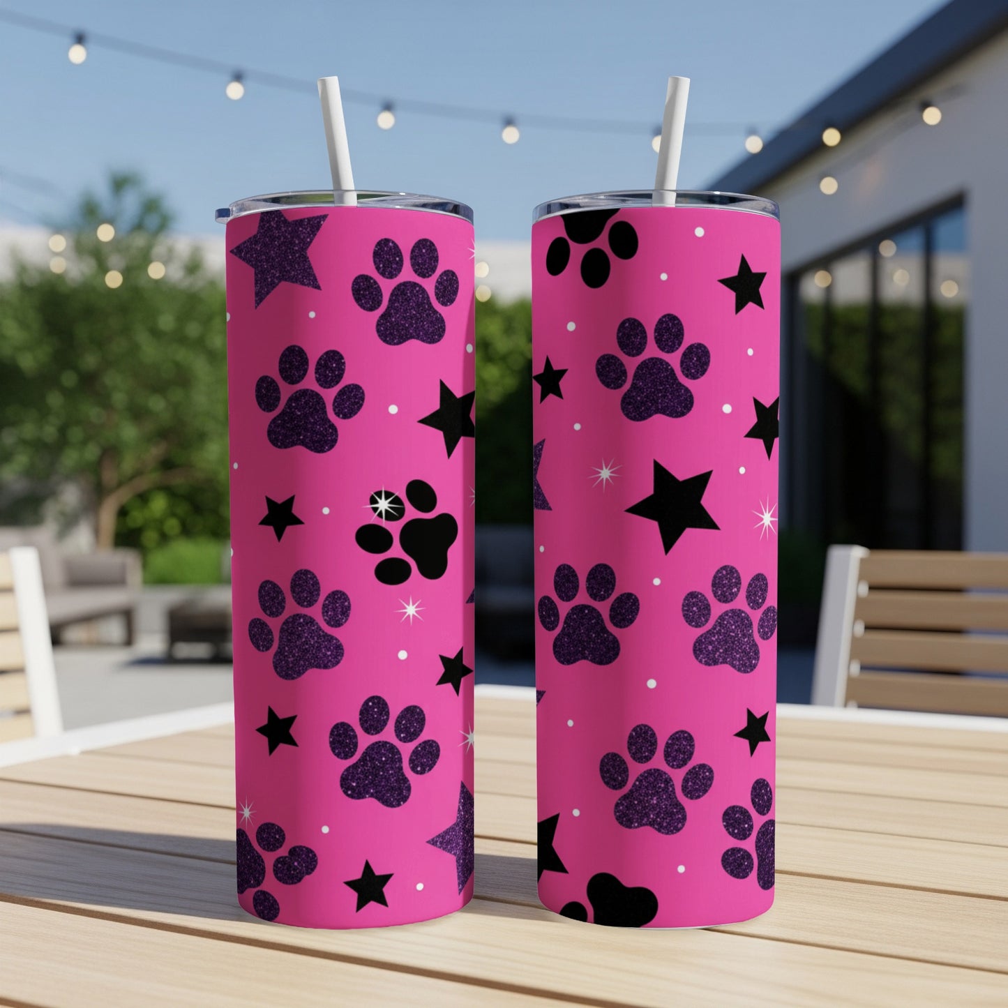 Two pink tumblers with black paw prints and stars on a patio table.