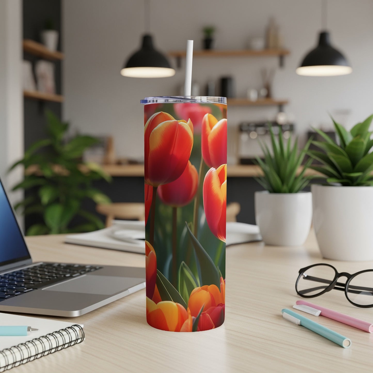 Tumbler with vibrant red and orange tulips, straw, laptop, and pens on desk.
