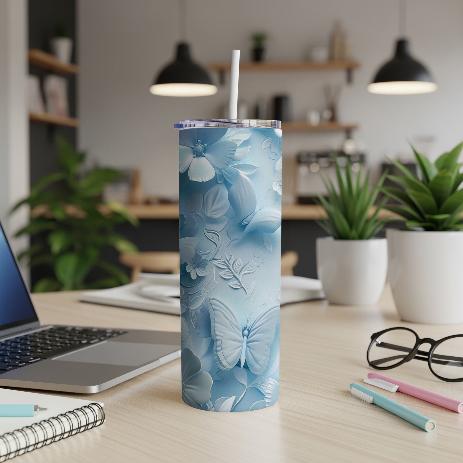 Blue floral and butterfly patterned tumbler with straw on desk.