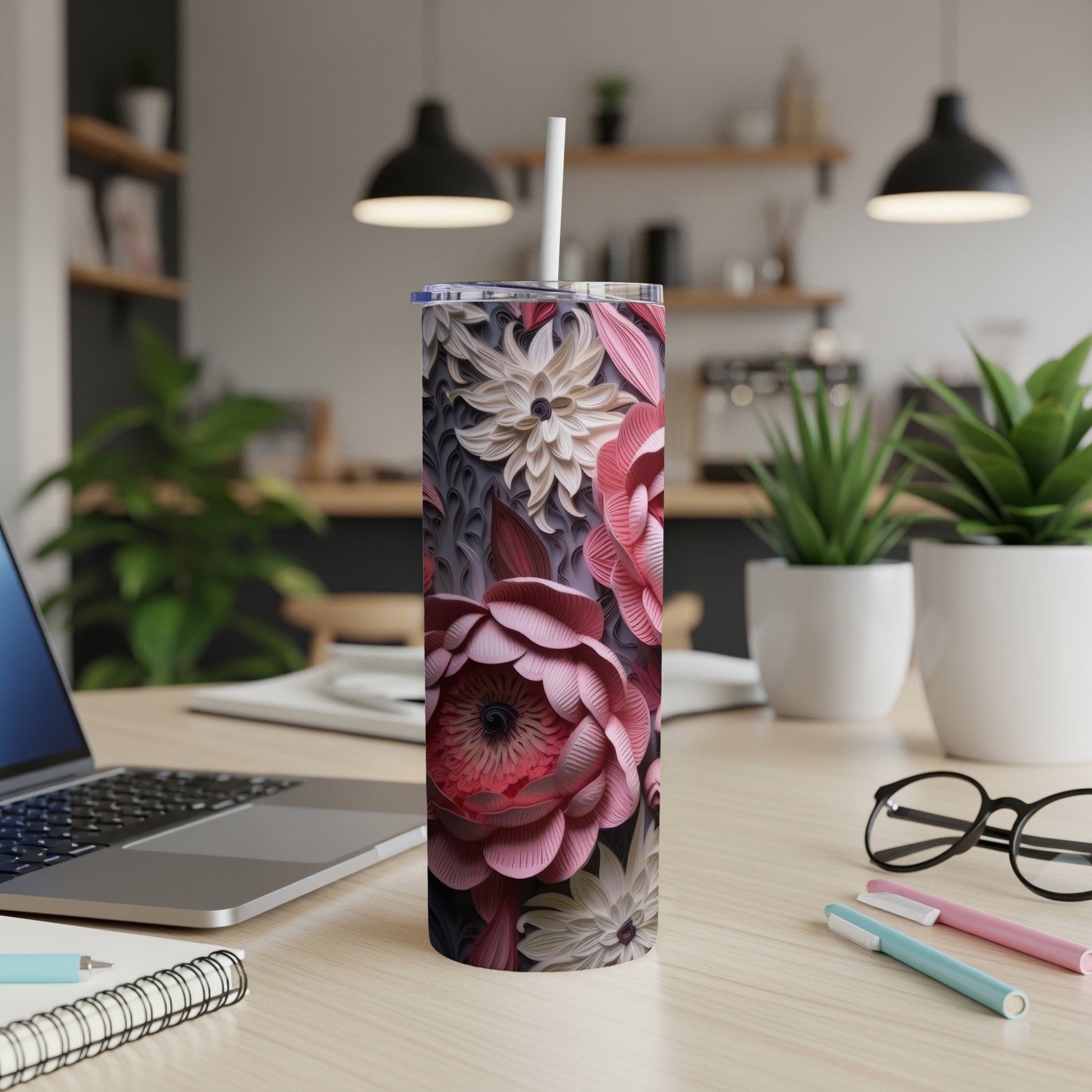 Floral-patterned tumbler with straw on a desk with a laptop and pens.