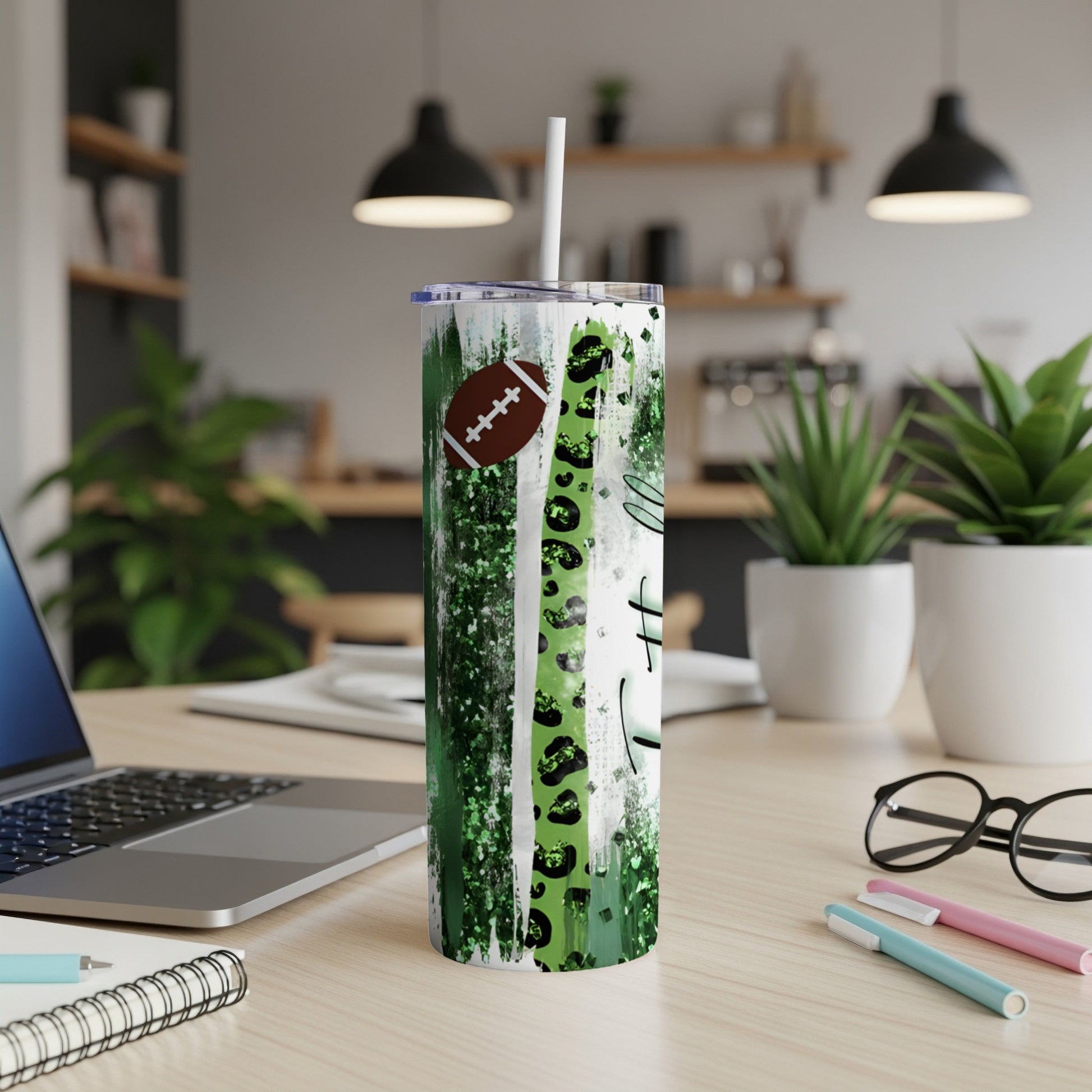 Green striped tumbler with football and white text, on a desk.