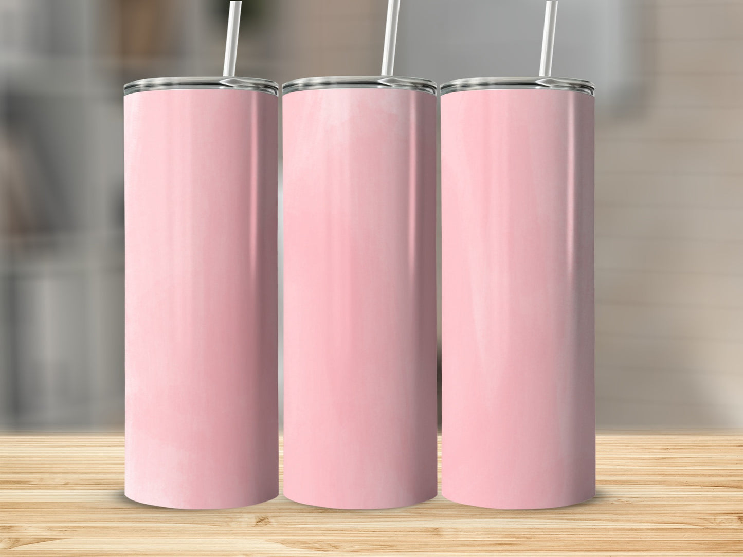 Three pink tumblers with white straws stand on a wooden surface.