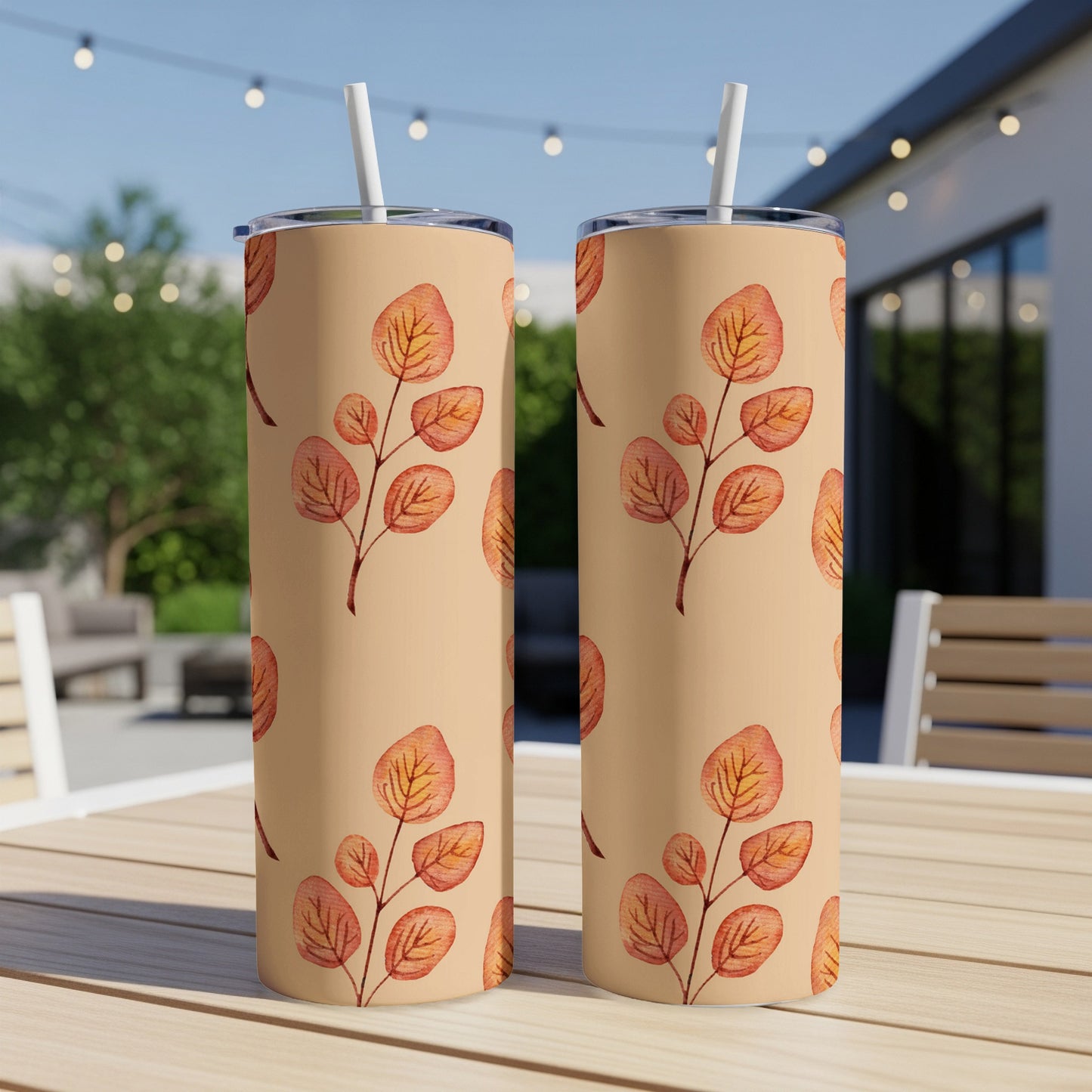 Two beige tumblers with orange and brown leaf pattern on a wooden table outdoors.